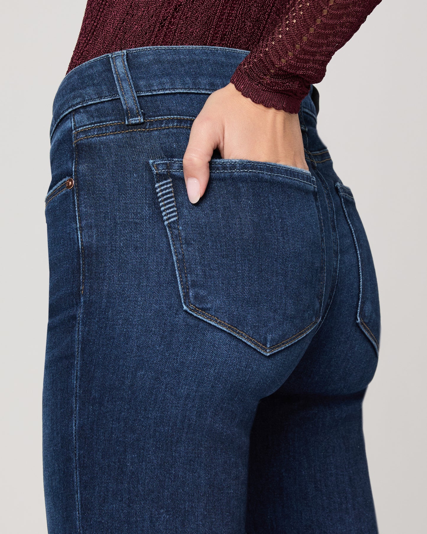 Woman wearing a burgundy top and blue jeans on a white background