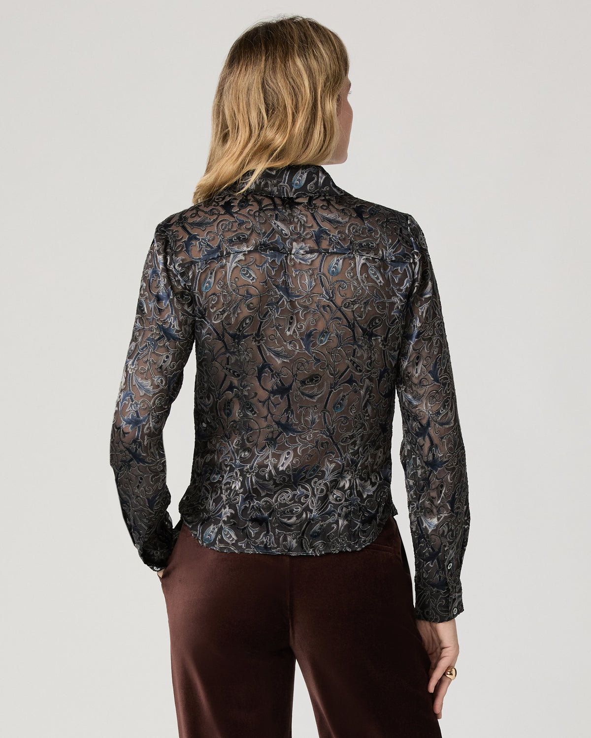 Women wearing a grey printed long sleeve top paired with suede burgundy jeans standing against a white background
