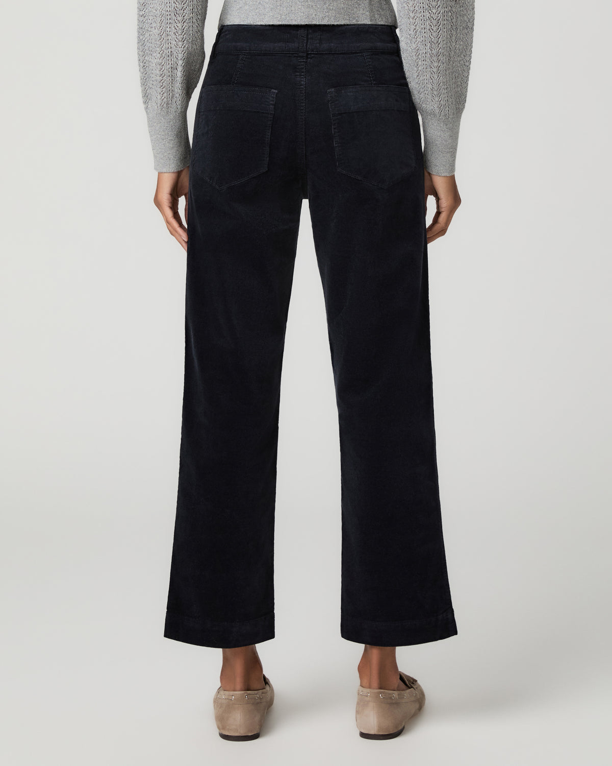 Close-up back view of navy corduroy ankle pants showing back patch pockets, paired with tan mule flats.