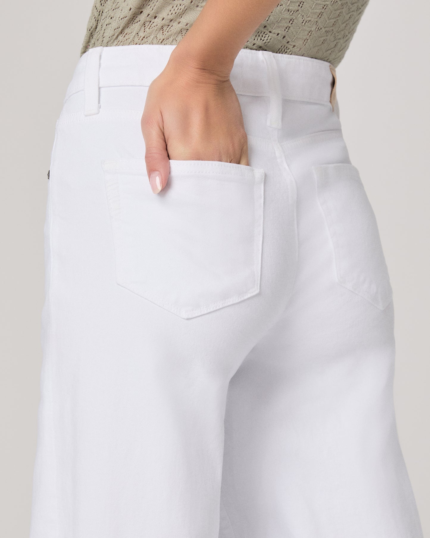 Woman wearing a green top and white pants on a plain background