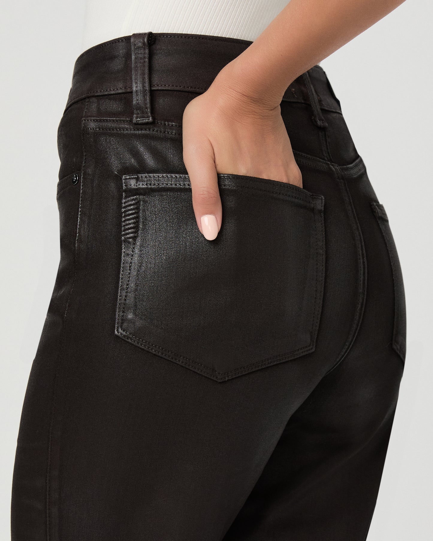A woman modeling an off-the-shoulder white top and black straight-leg jeans against a light gray studio background.