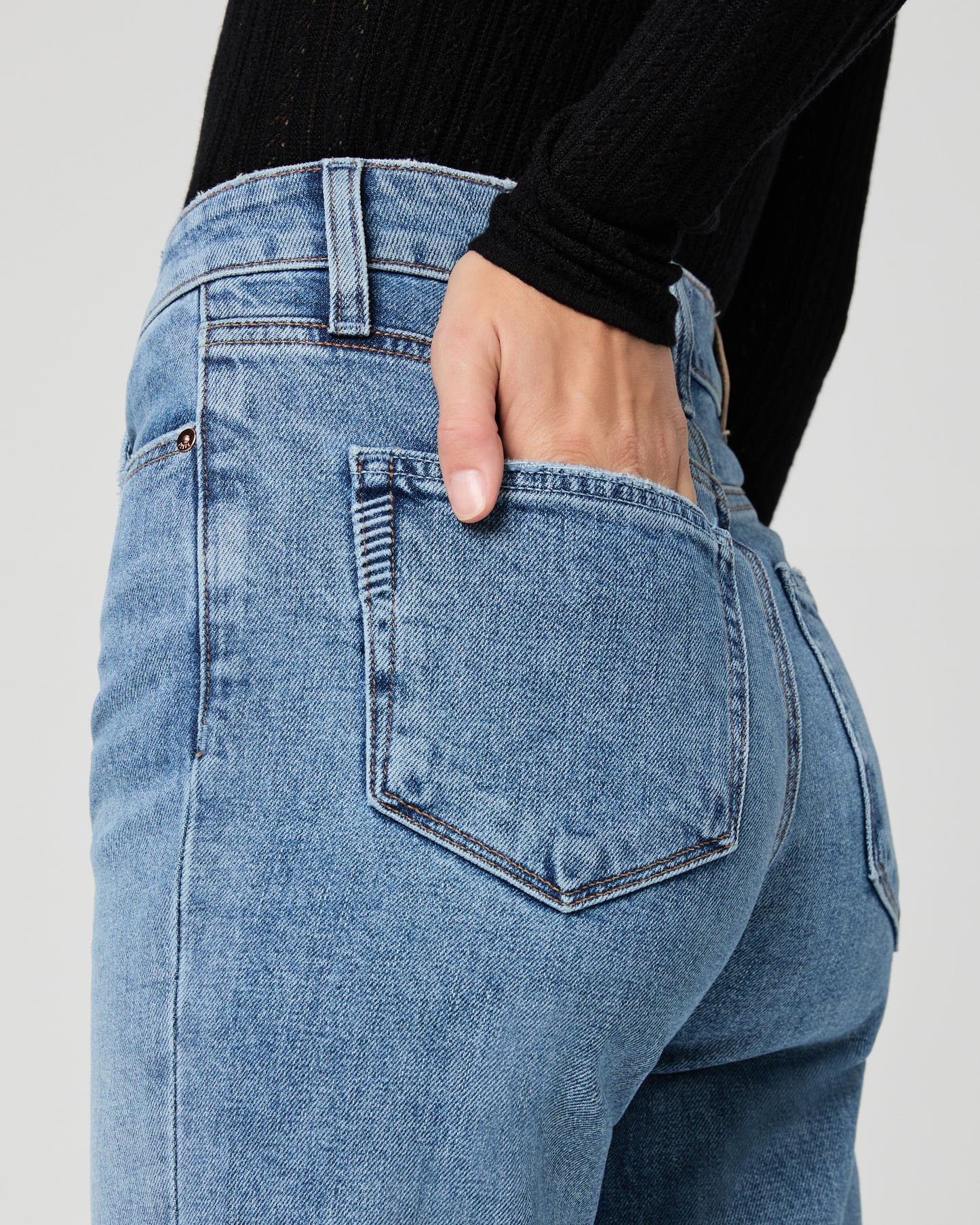 Close-up of blue jeans with a hand in the pocket on a light gray background