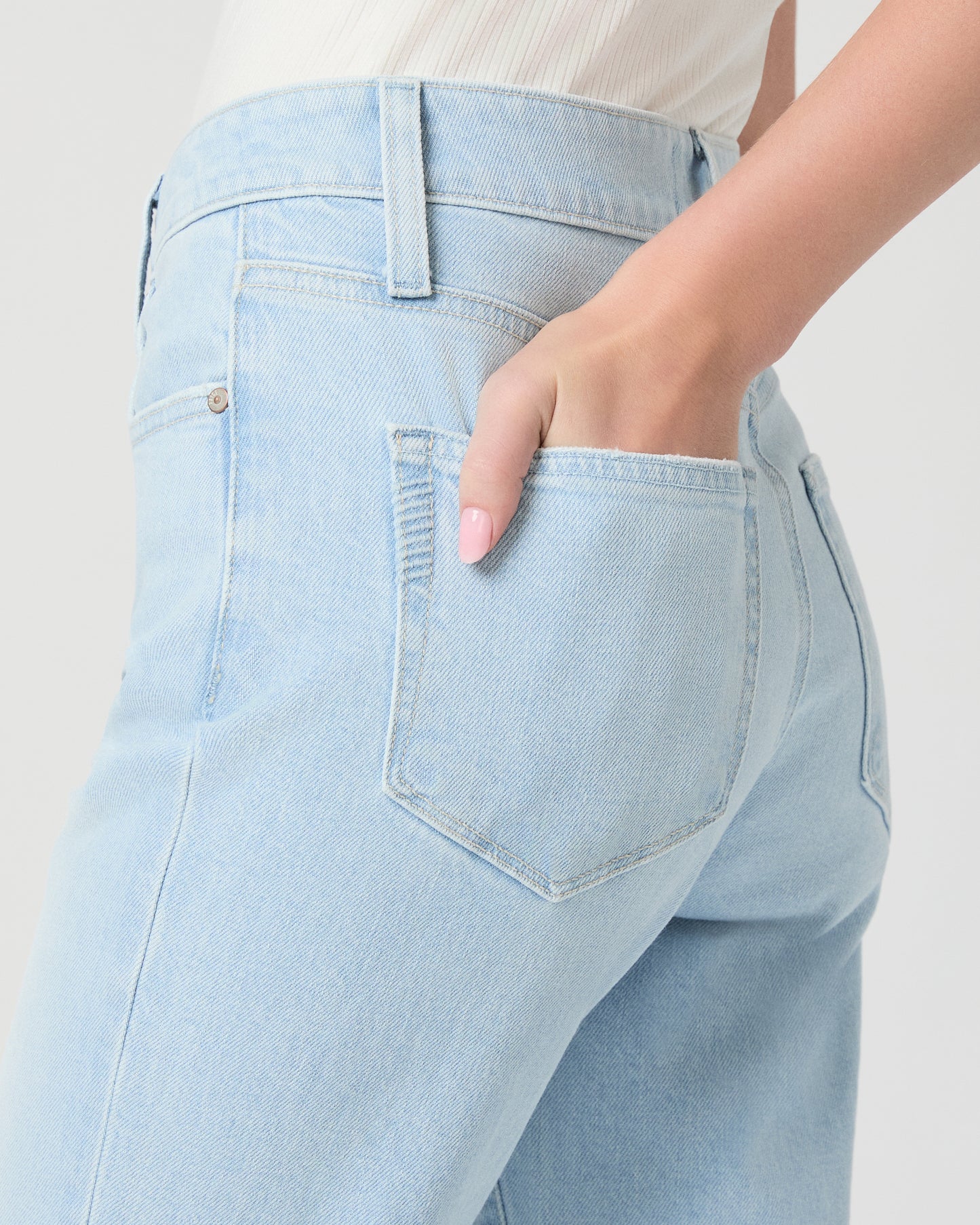 Woman wearing light blue jeans and a white off-shoulder top on a white background