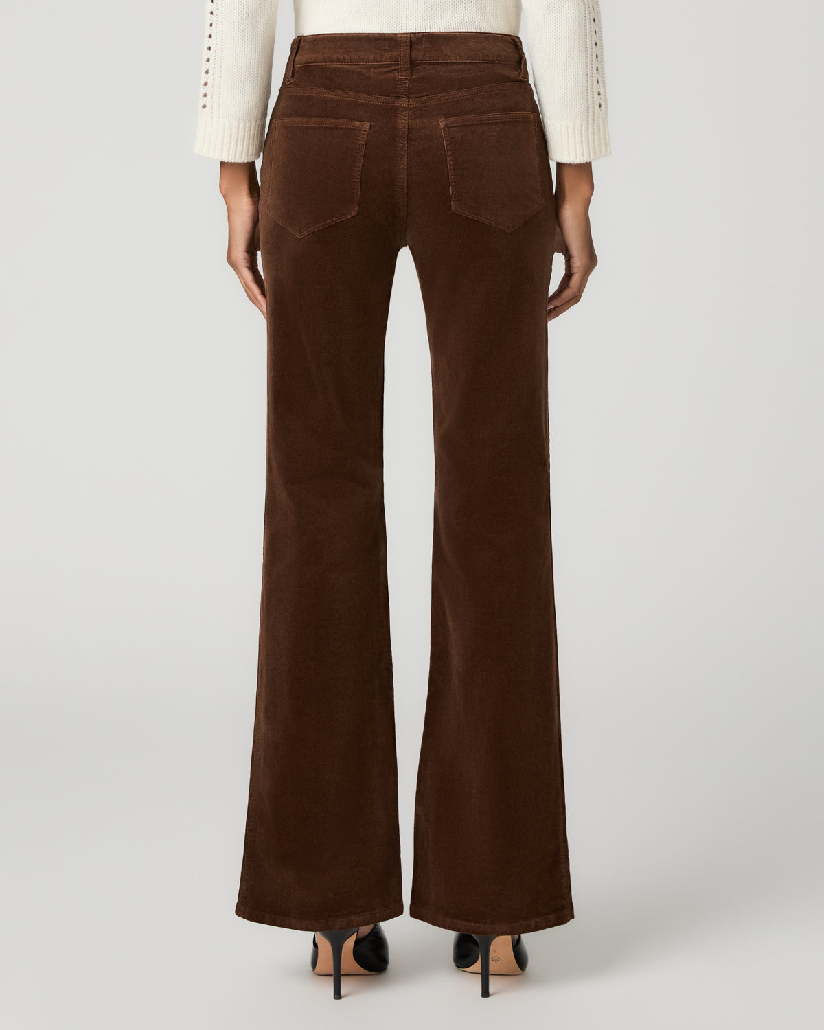 Close-up back view of hickory brown corduroy flare pants showing a back patch pocket, paired with black ankle-strap heels.
