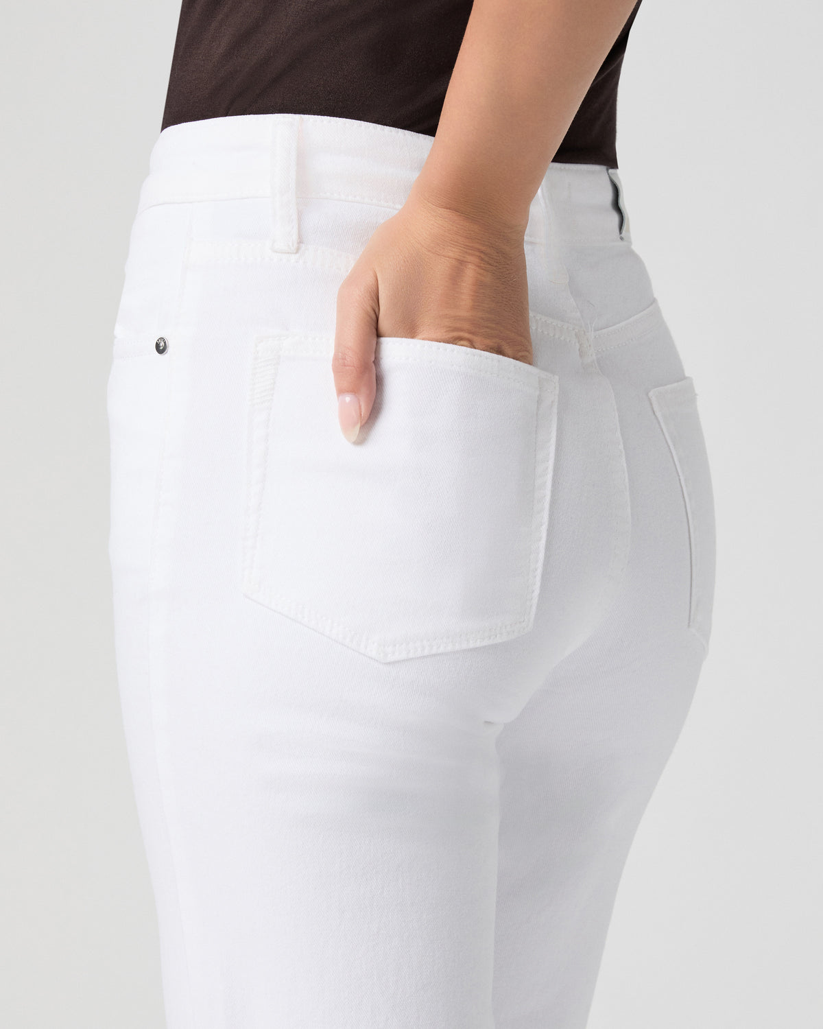 Close-up of the back pocket of Stevie Ankle Straight Jeans in Radiant White, model's hand tucked into the pocket, brown top visible