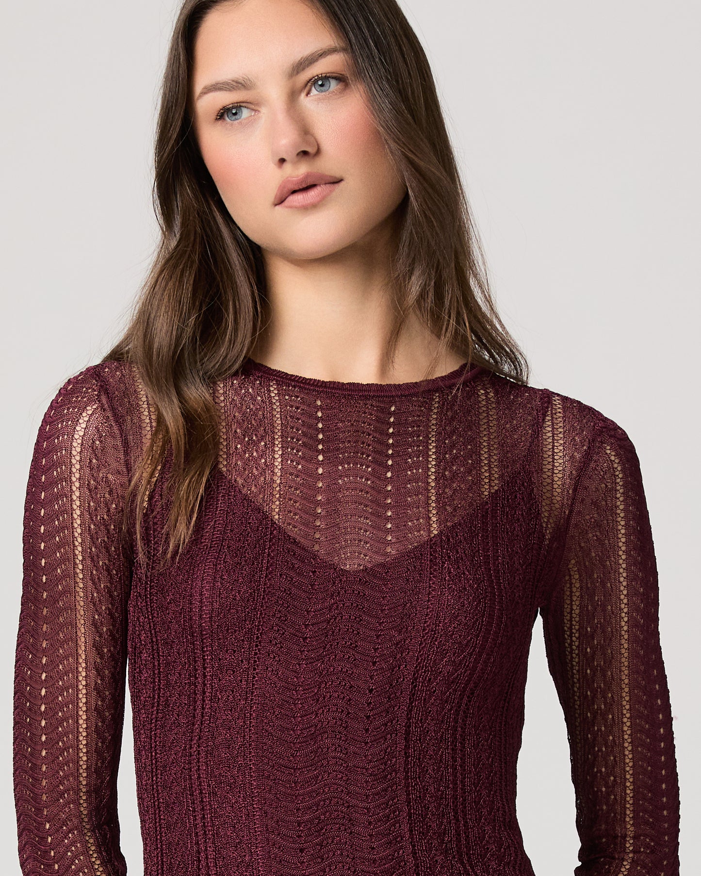 Woman wearing a maroon sweater with intricate patterns on a plain background