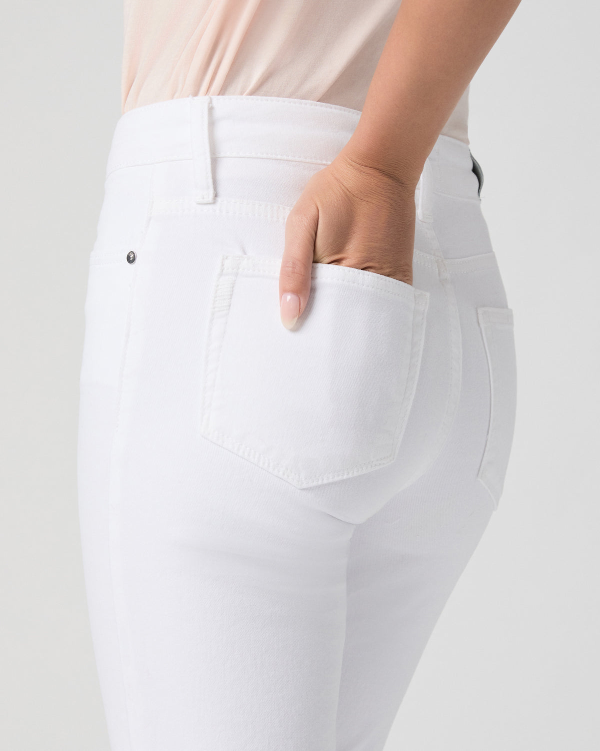 Close-up of the back pocket of Mason Crop Bootcut Jeans in Radiant White, model's hand tucked into the pocket, blush top visible