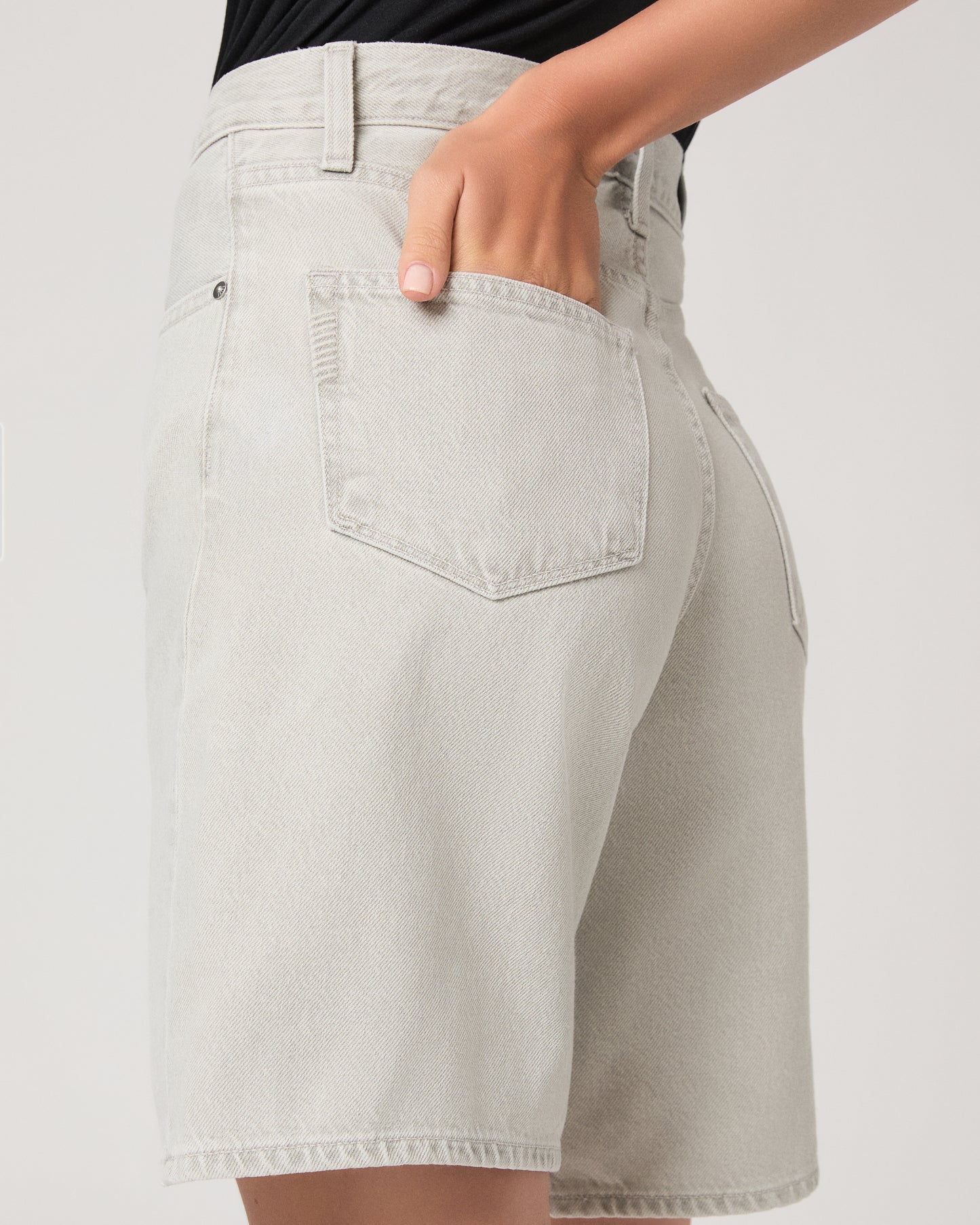 Woman wearing a black top and grey shorts on a white background
