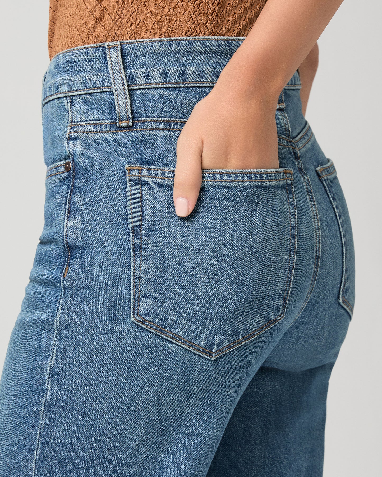 Women wearing a brown color top paired with medium wash denim and brown heels against a white background