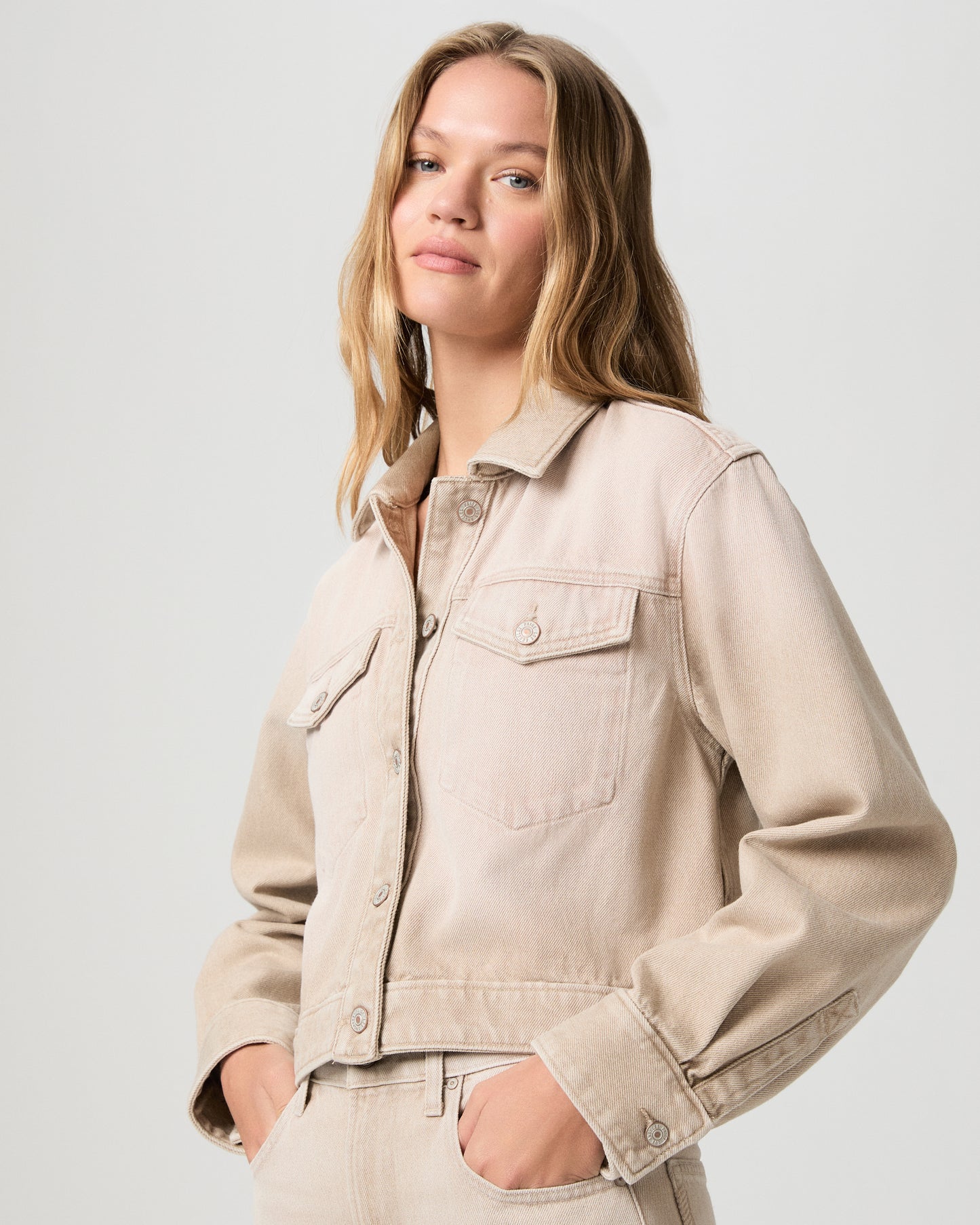 Woman wearing a beige denim jacket against a plain background