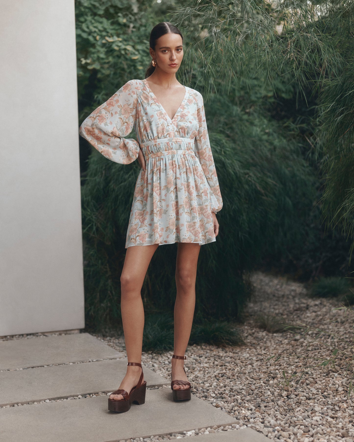 Woman in a floral dress standing outdoors with greenery in the background