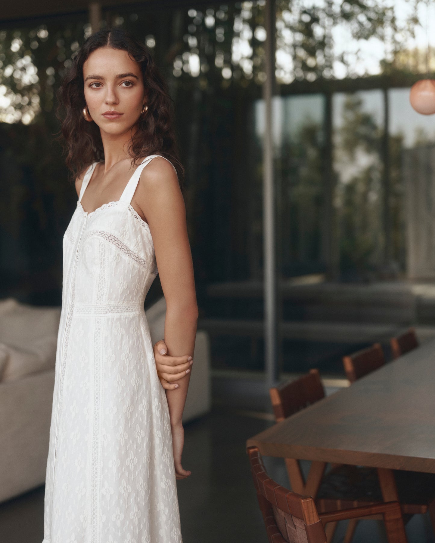 Woman in a white dress standing in a modern indoor setting with large windows.