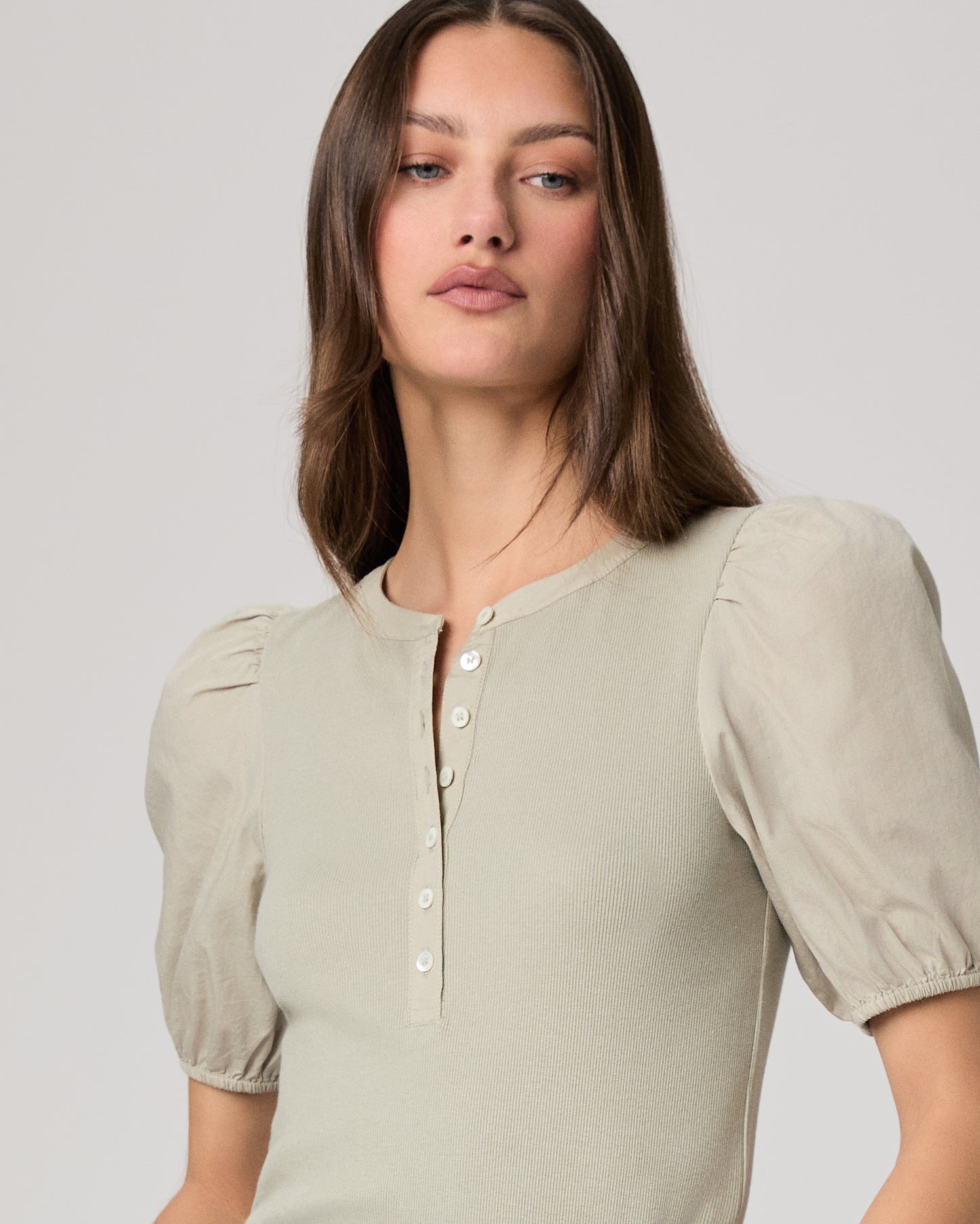 Woman wearing a light green blouse with puffed sleeves and blue jeans on a plain background