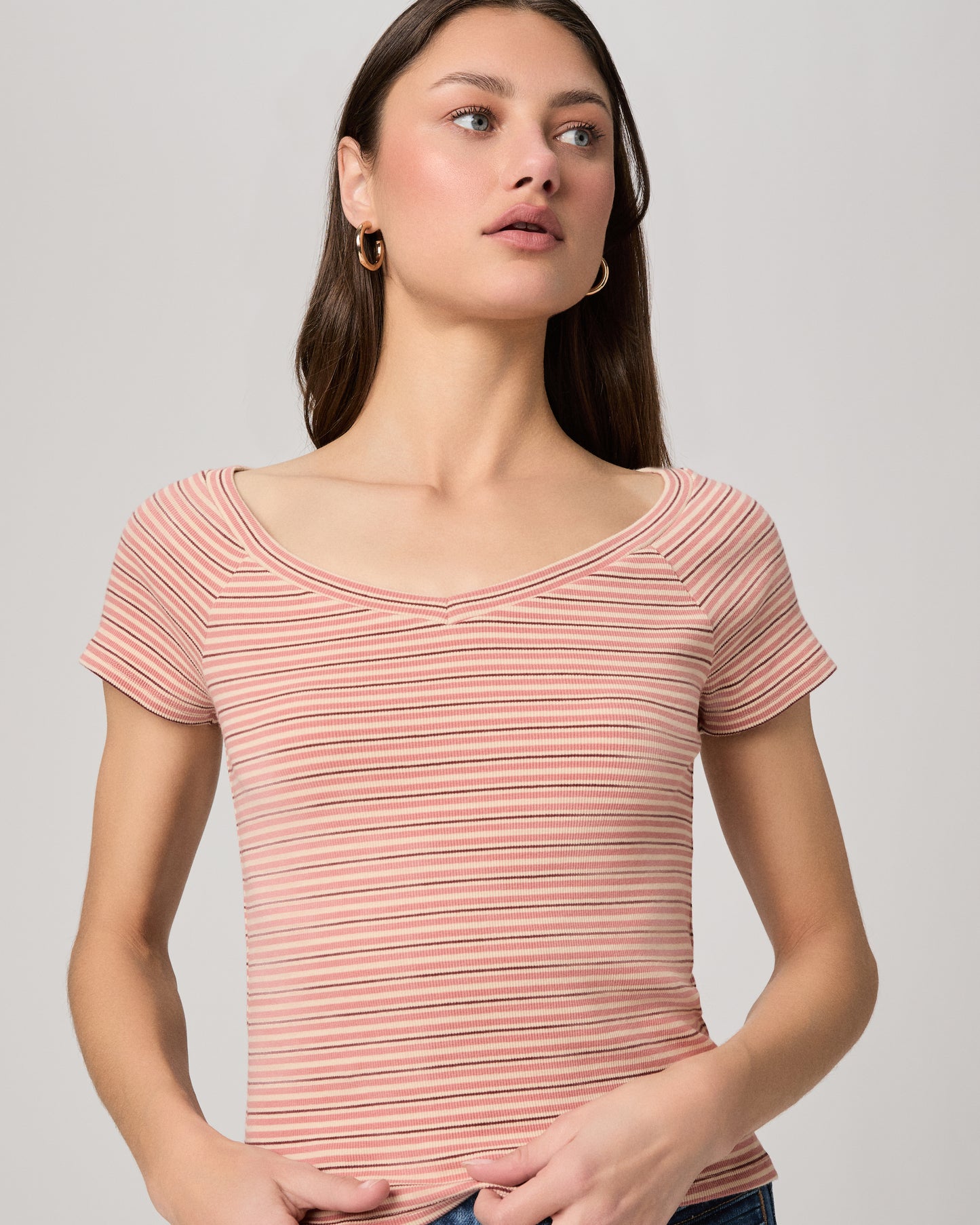 Woman wearing a striped pink top and blue jeans on a plain background