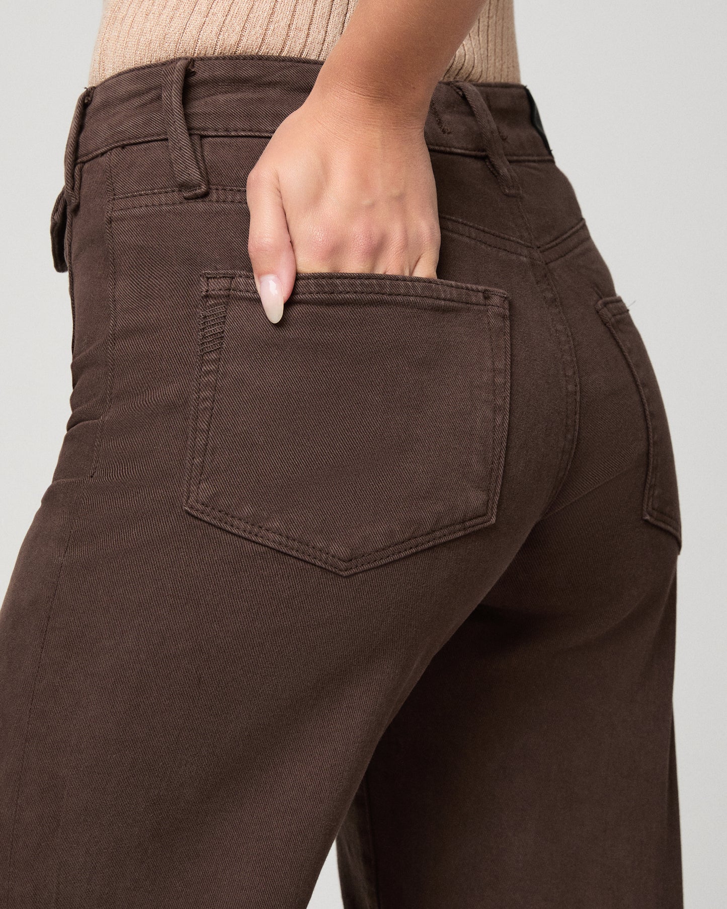 Woman in cream top and brown pants with a white background