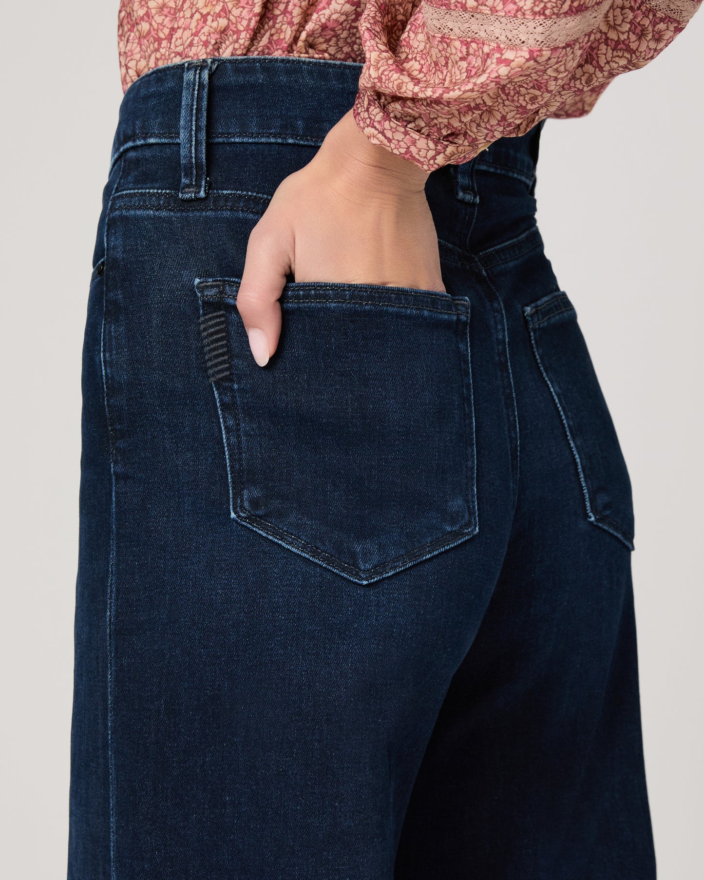Woman wearing a pink blouse and dark blue jeans on a white background