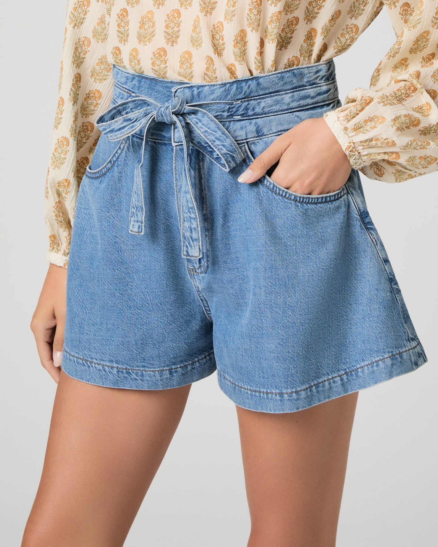 Woman wearing a patterned blouse and denim shorts on a white background