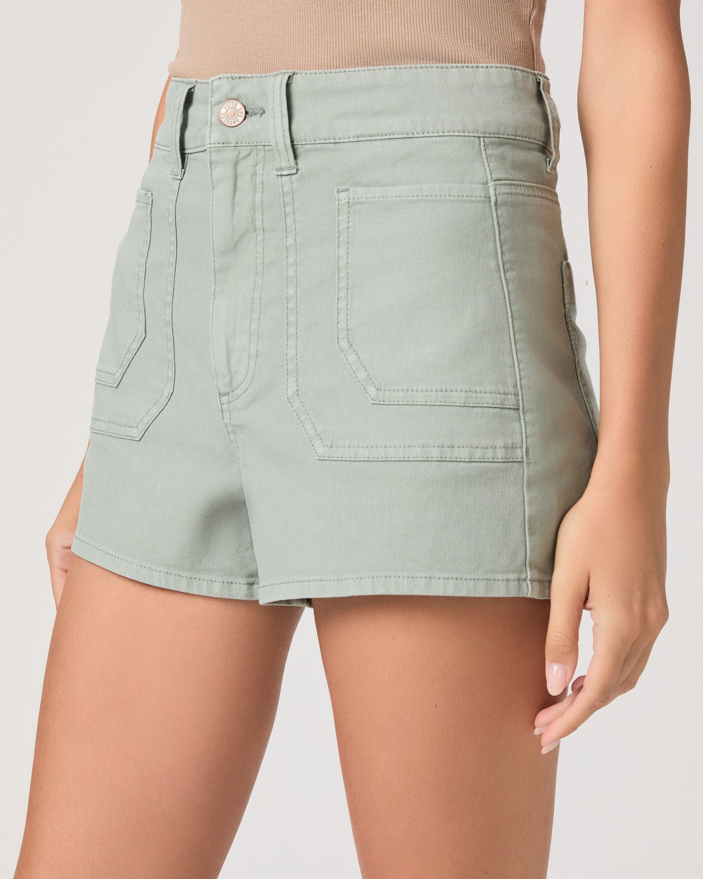 Woman wearing a beige tank top and light green shorts on a white background