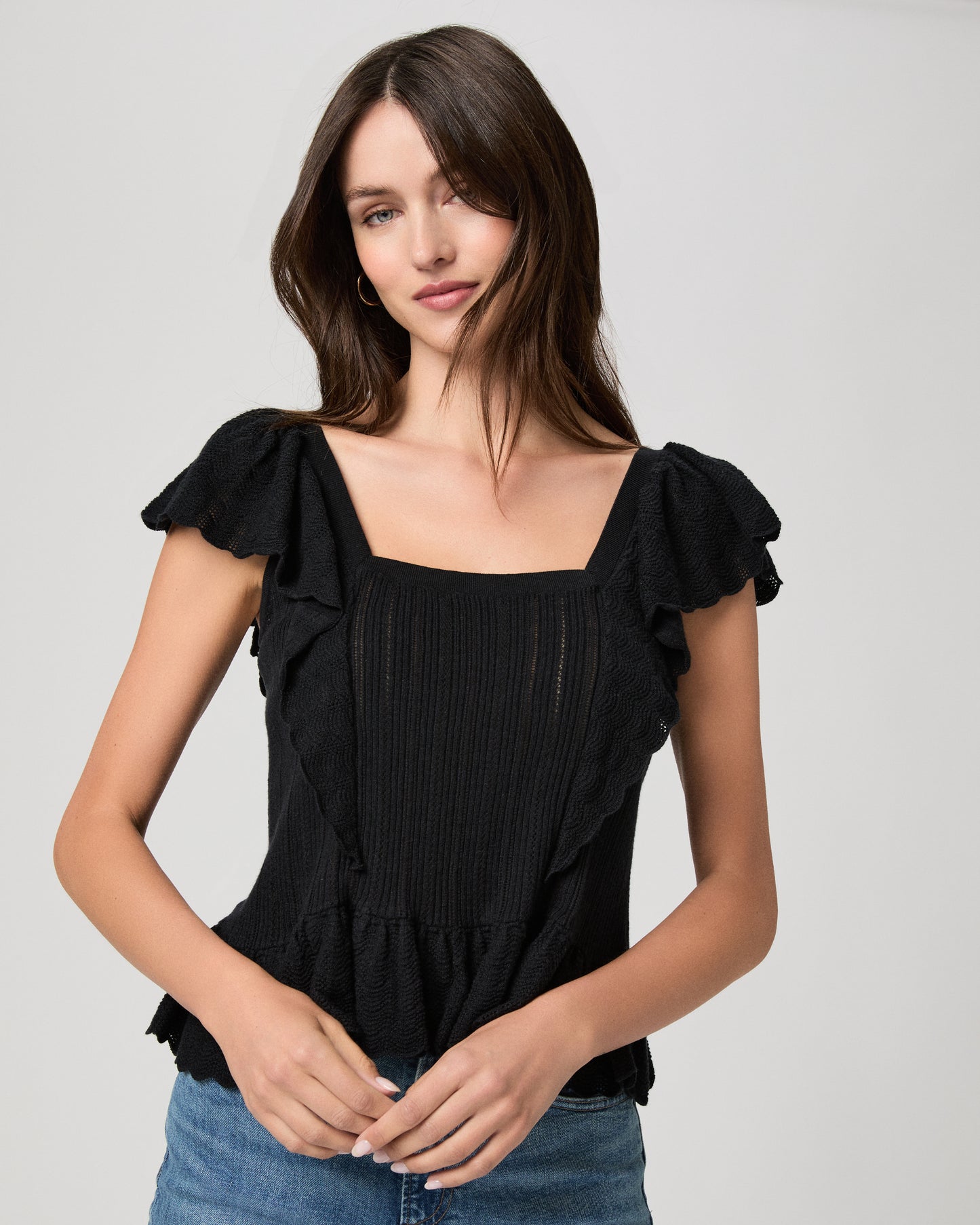 Woman wearing a black ruffled top and blue jeans on a gray background