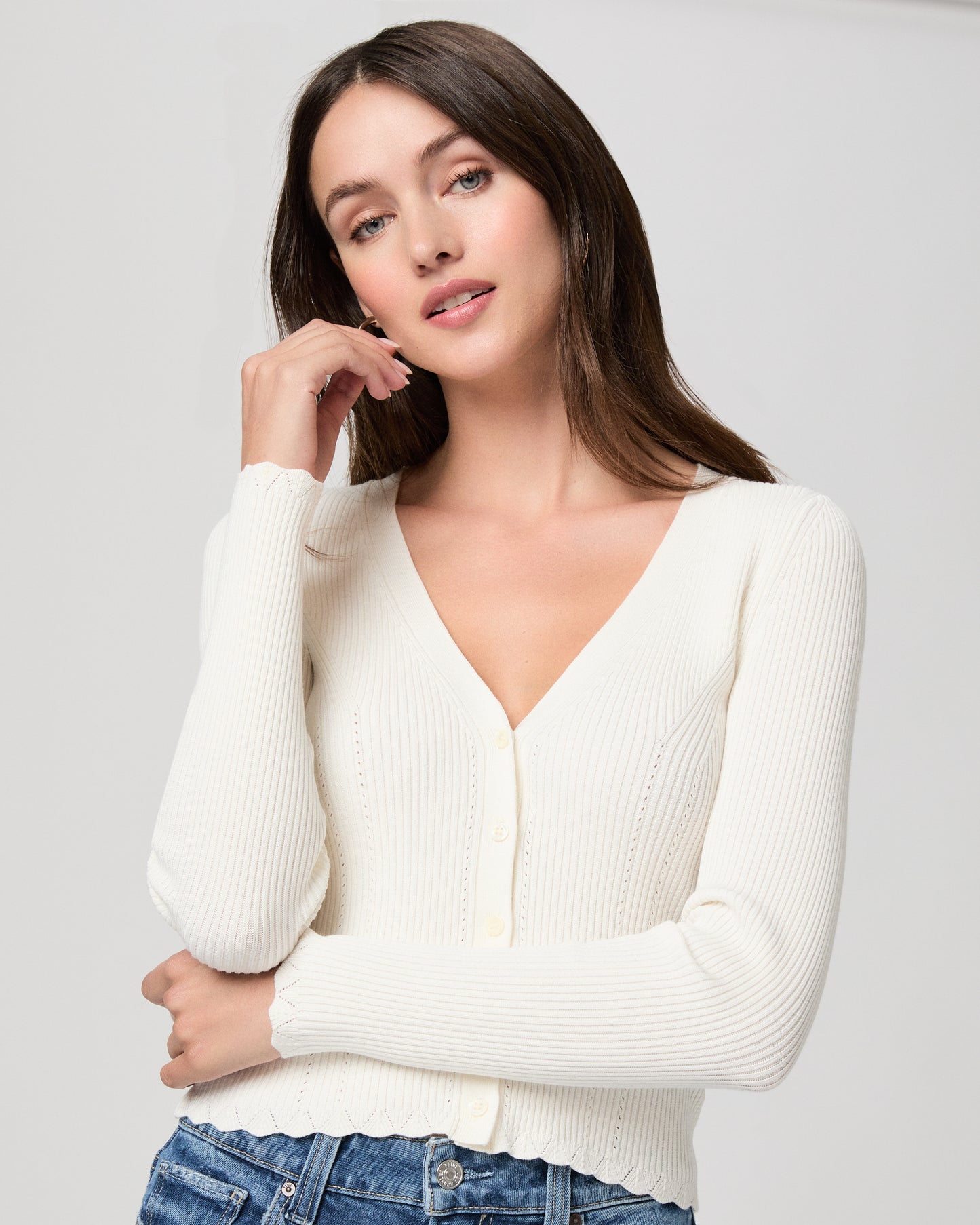 Woman wearing a white sweater and blue jeans on a plain background
