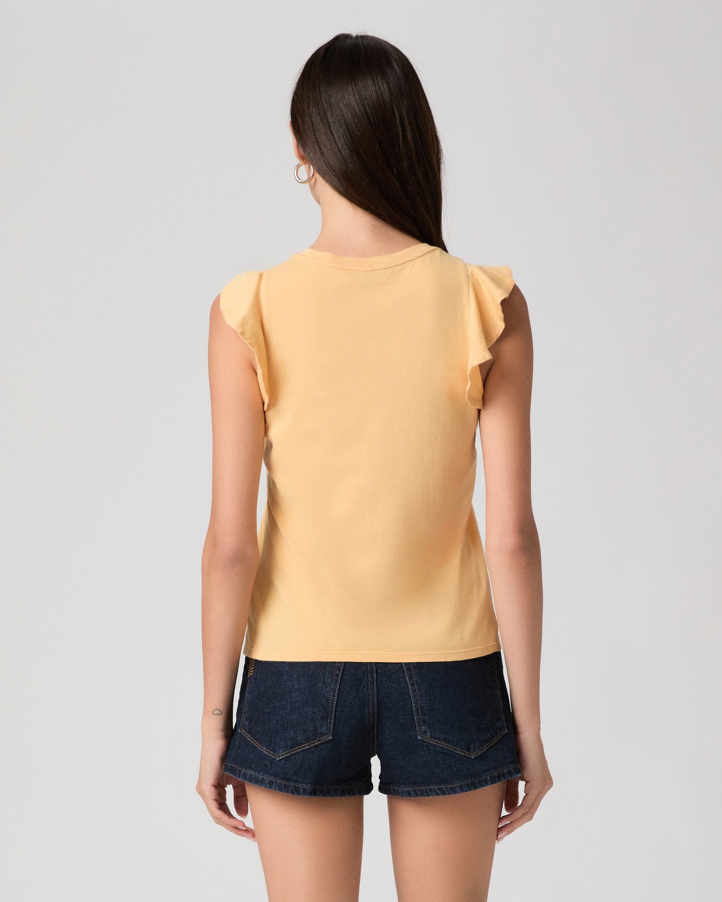 Woman wearing a yellow sleeveless top and denim shorts on a plain background