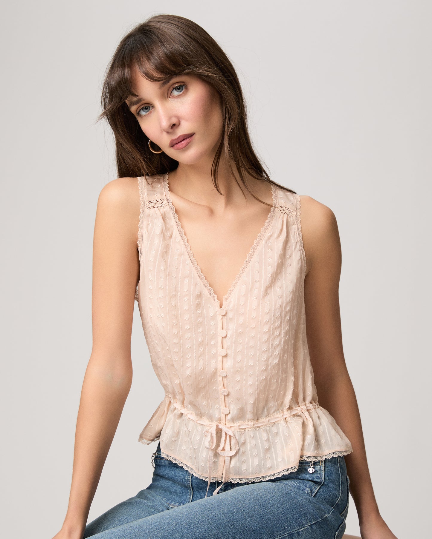 Woman wearing a light pink sleeveless top and blue jeans on a plain background