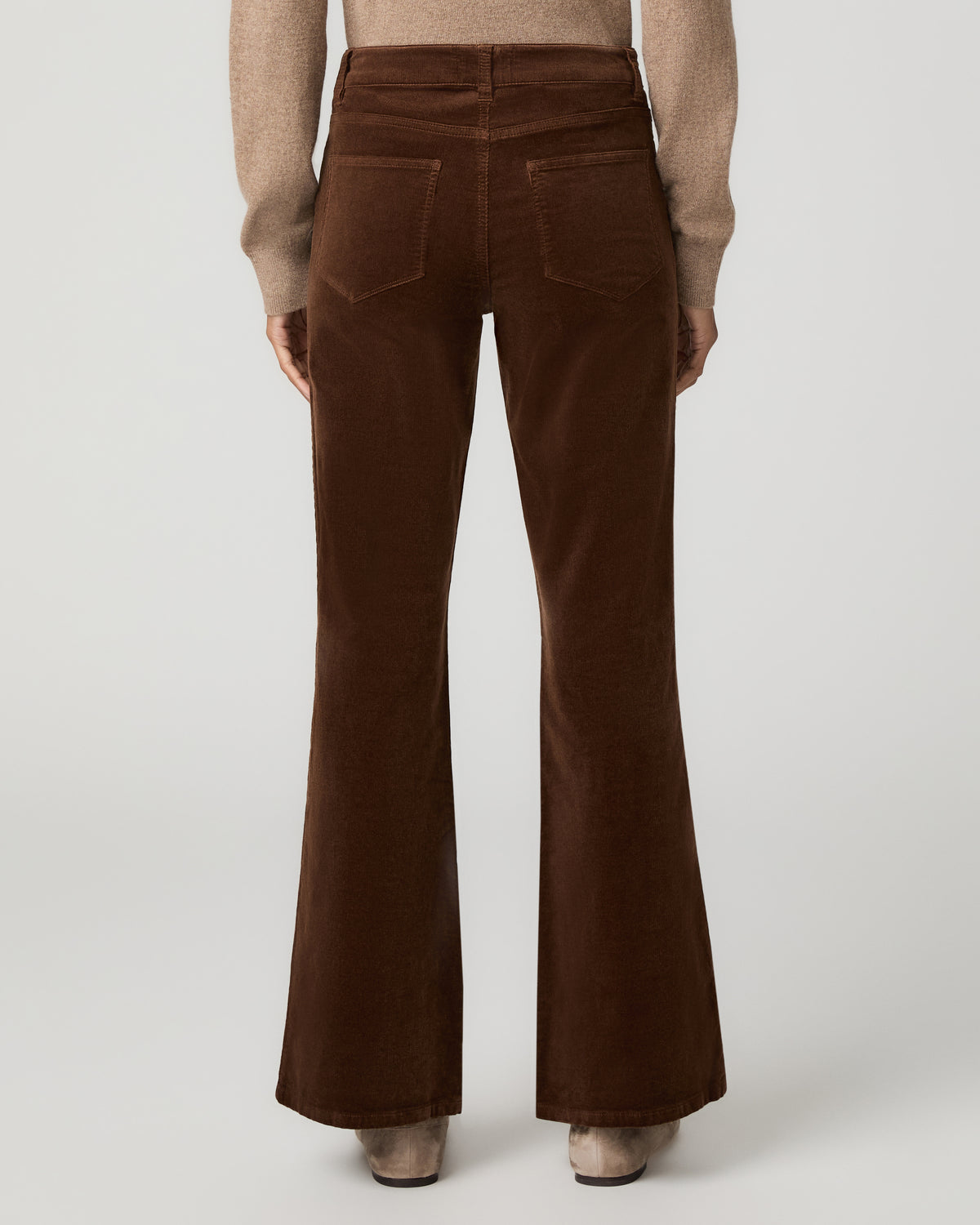 Close-up back view of hickory brown corduroy flare pants showing back patch pockets, paired with a tan sweater and tan flats.