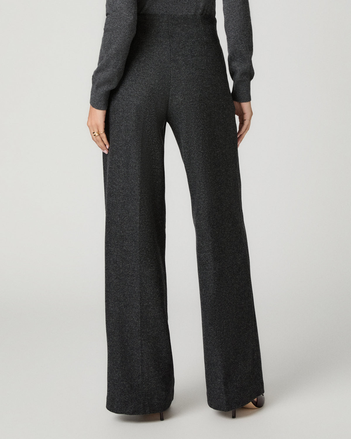 A person shown from the back wearing dark charcoal gray wide-leg trousers and a matching long-sleeve top against a light gray studio background.