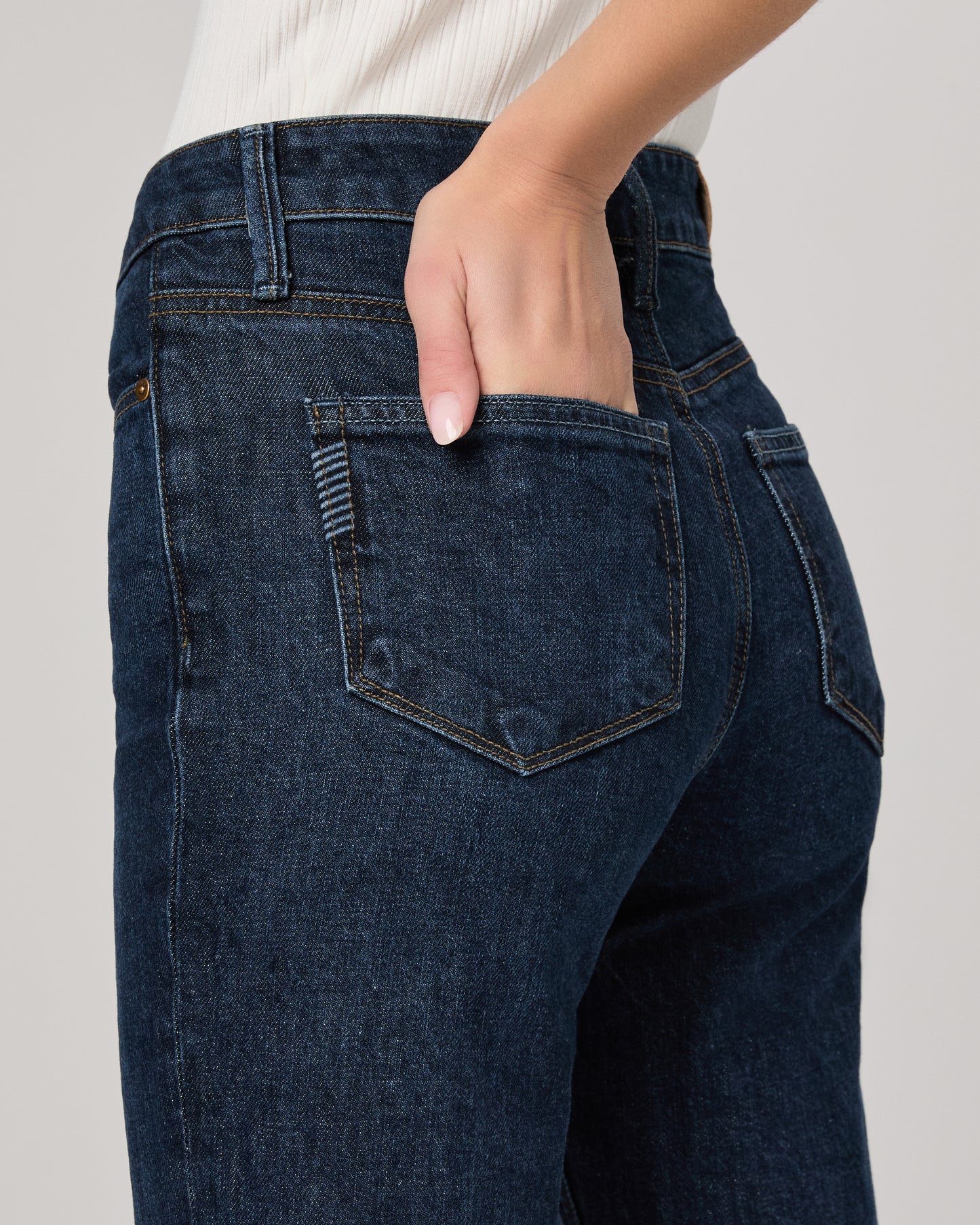 Dark blue jeans with a hand in the pocket on a light gray background