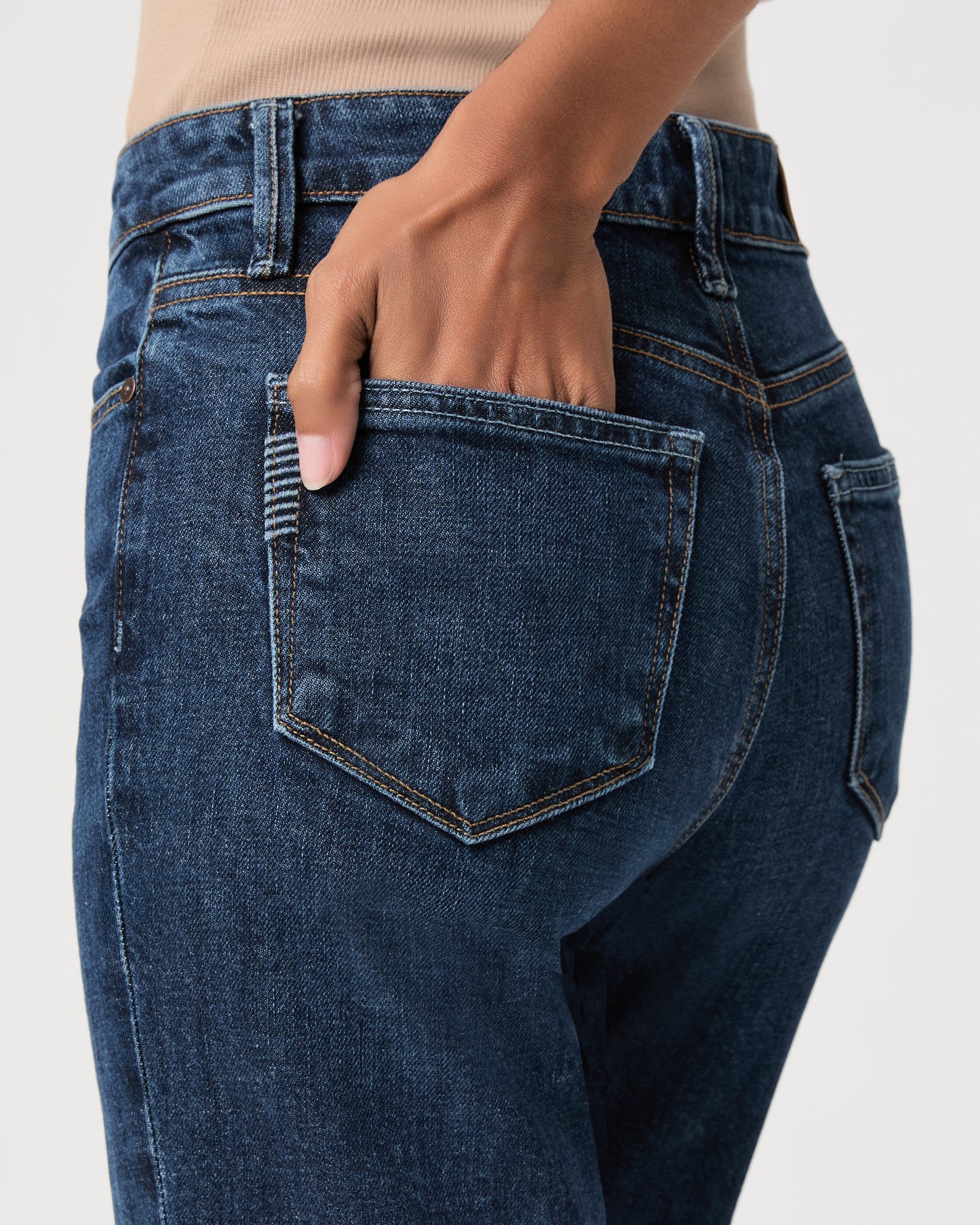 women wearing a beige top paired with dark wash jeans against a white background