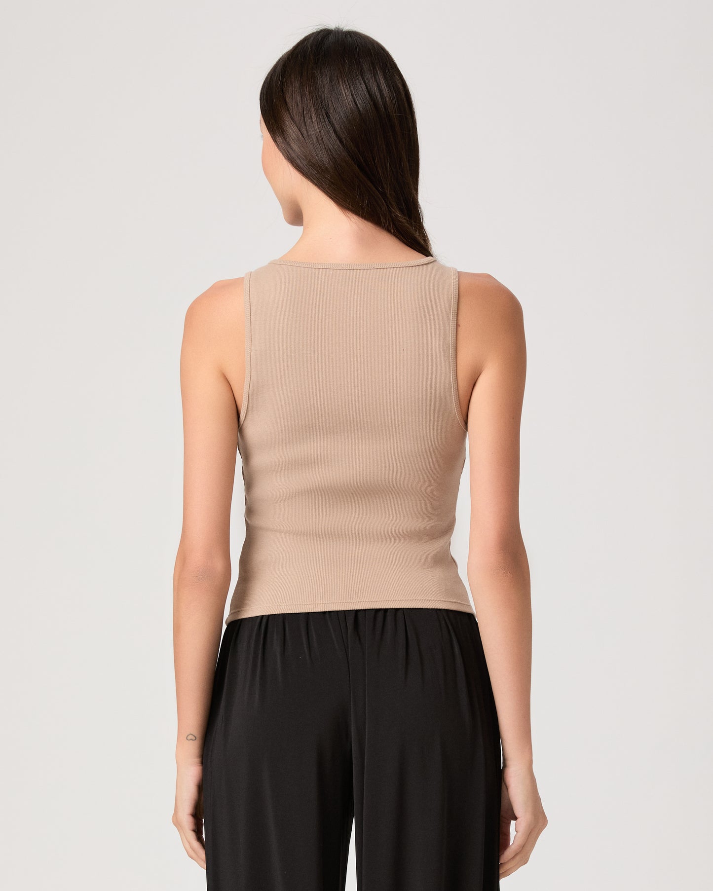 Model wearing a beige tank top paired with black pants