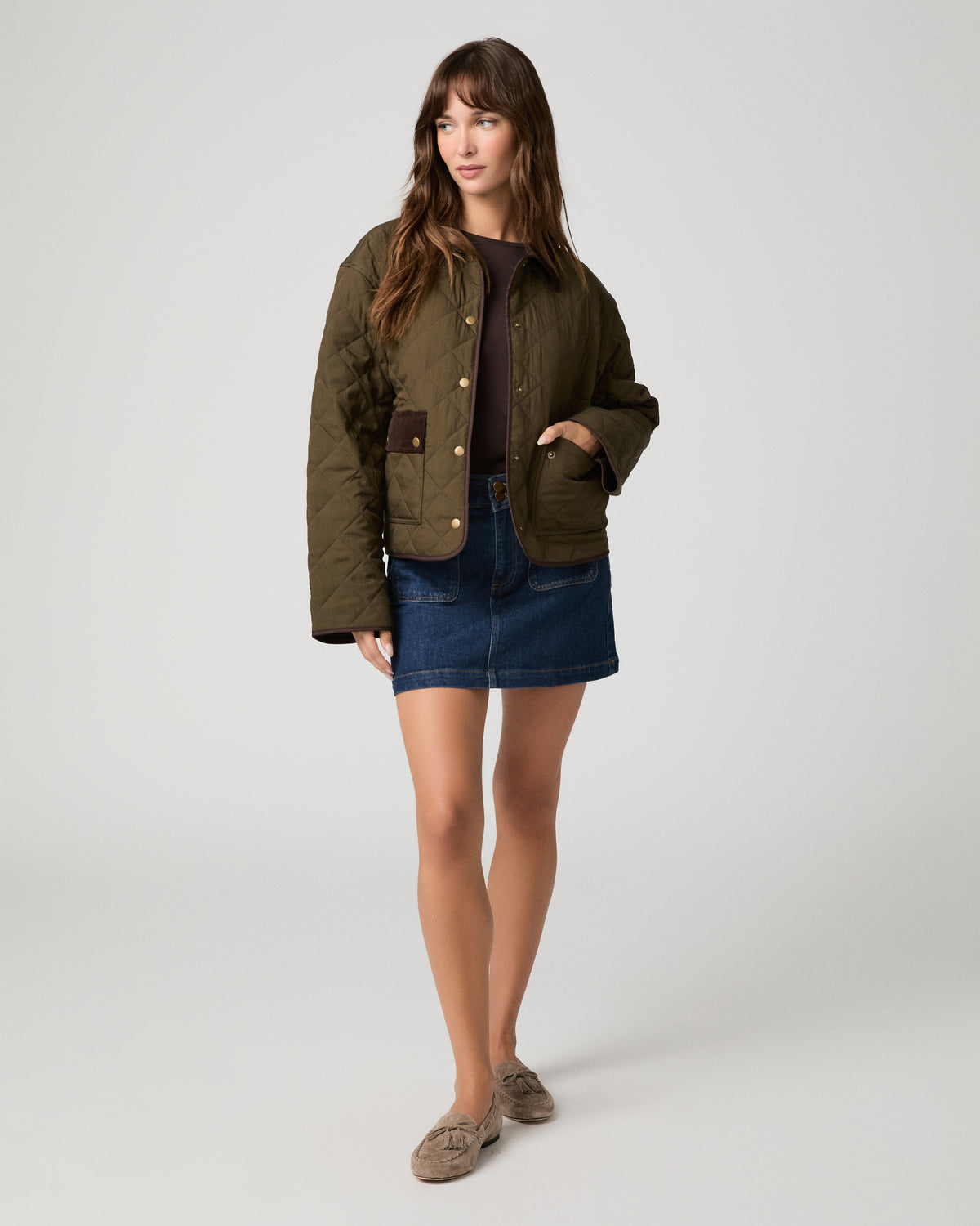 Woman wearing a brown top paired with a green jacket and denim skirt against a white background