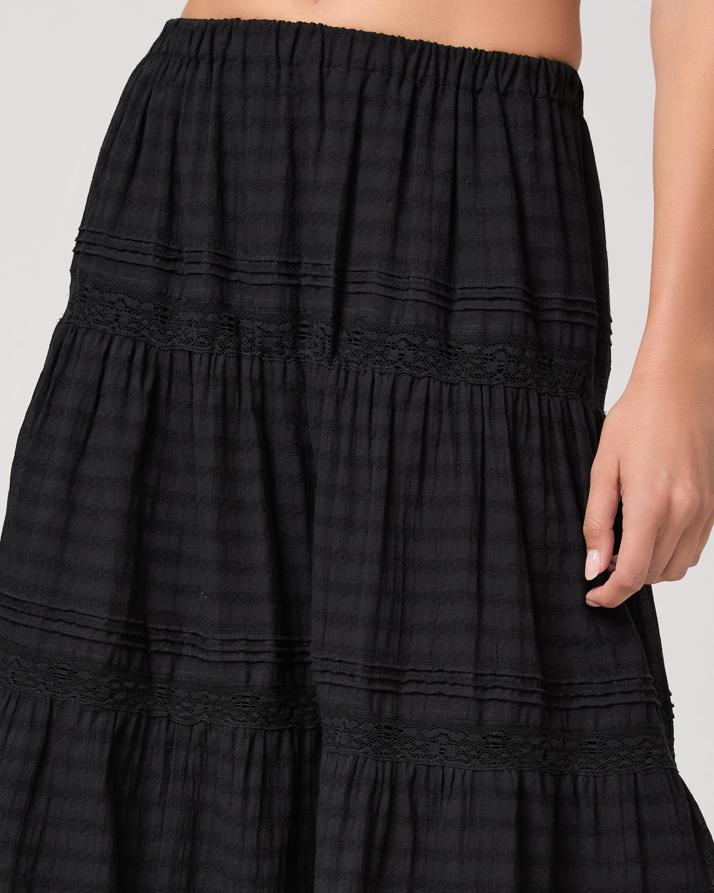 Model wearing a black midi skirt paired with a black top and gold sandals