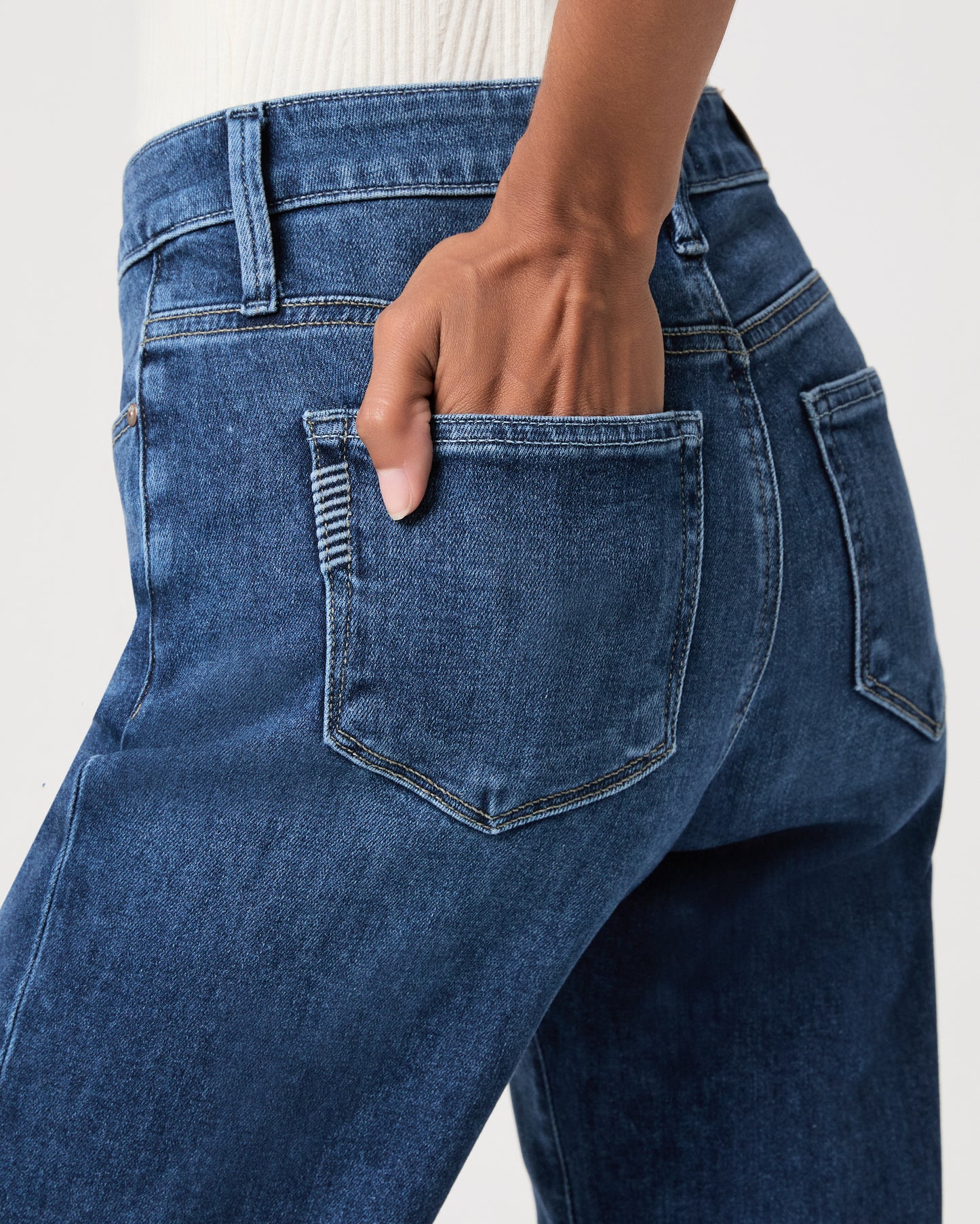 Woman wearing a white top paired with medium wash jeans and gold wedges against a white background