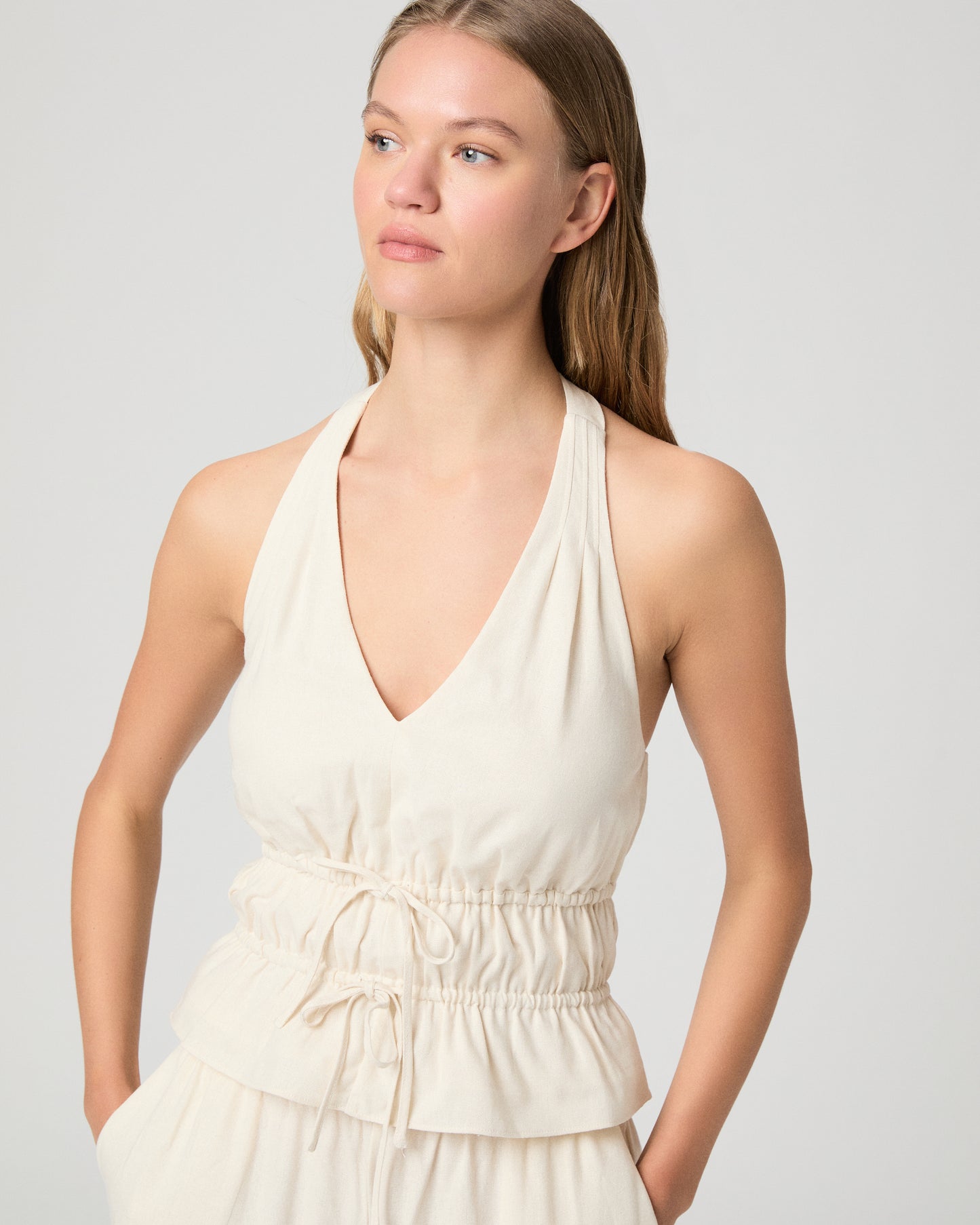 Woman wearing a white halter neck top and white pants against a plain background