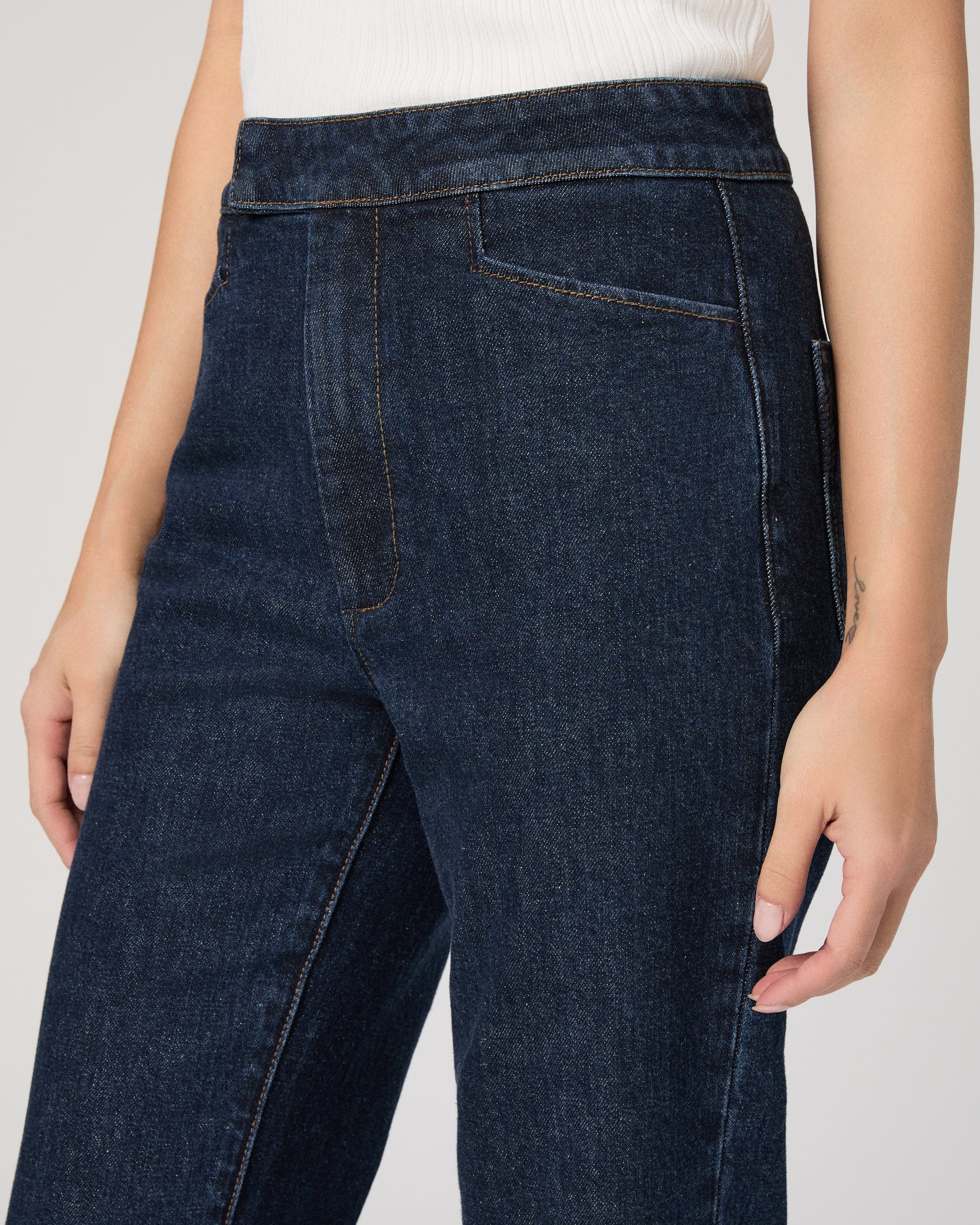 Woman wearing a white sleeveless top and dark blue jeans on white background
