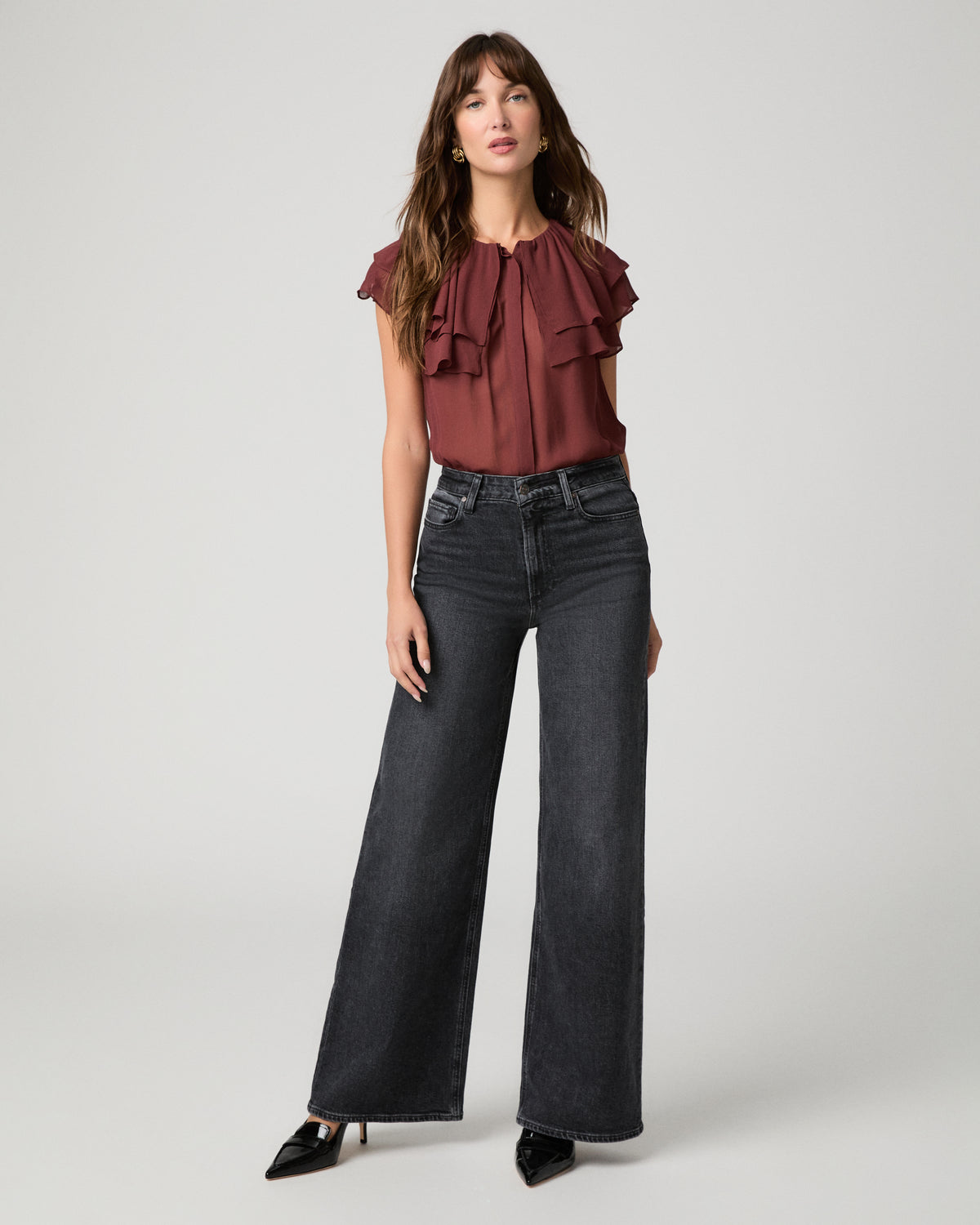 Woman wearing maroon top and black jeans against a white background