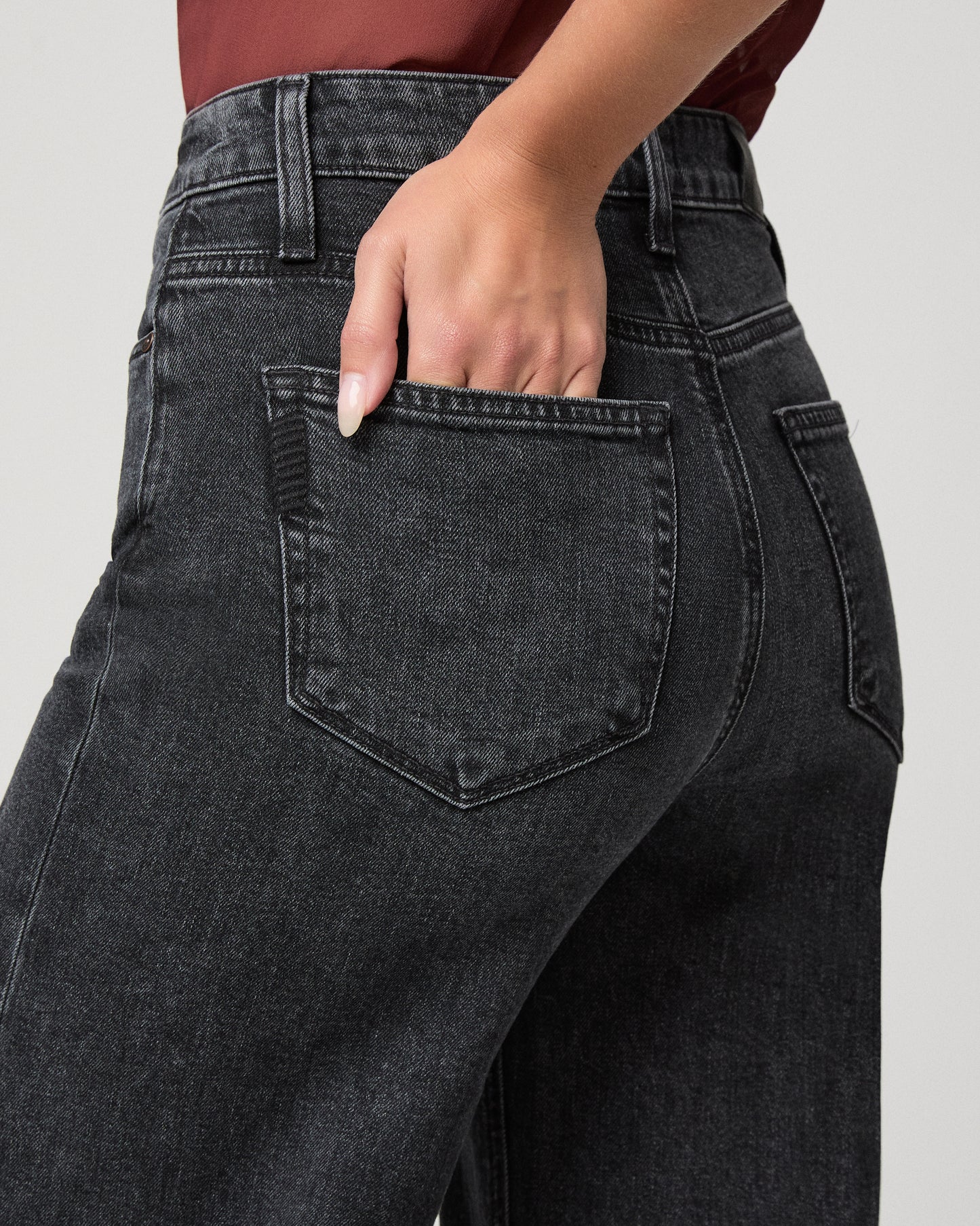 Woman wearing maroon top and black jeans against a white background