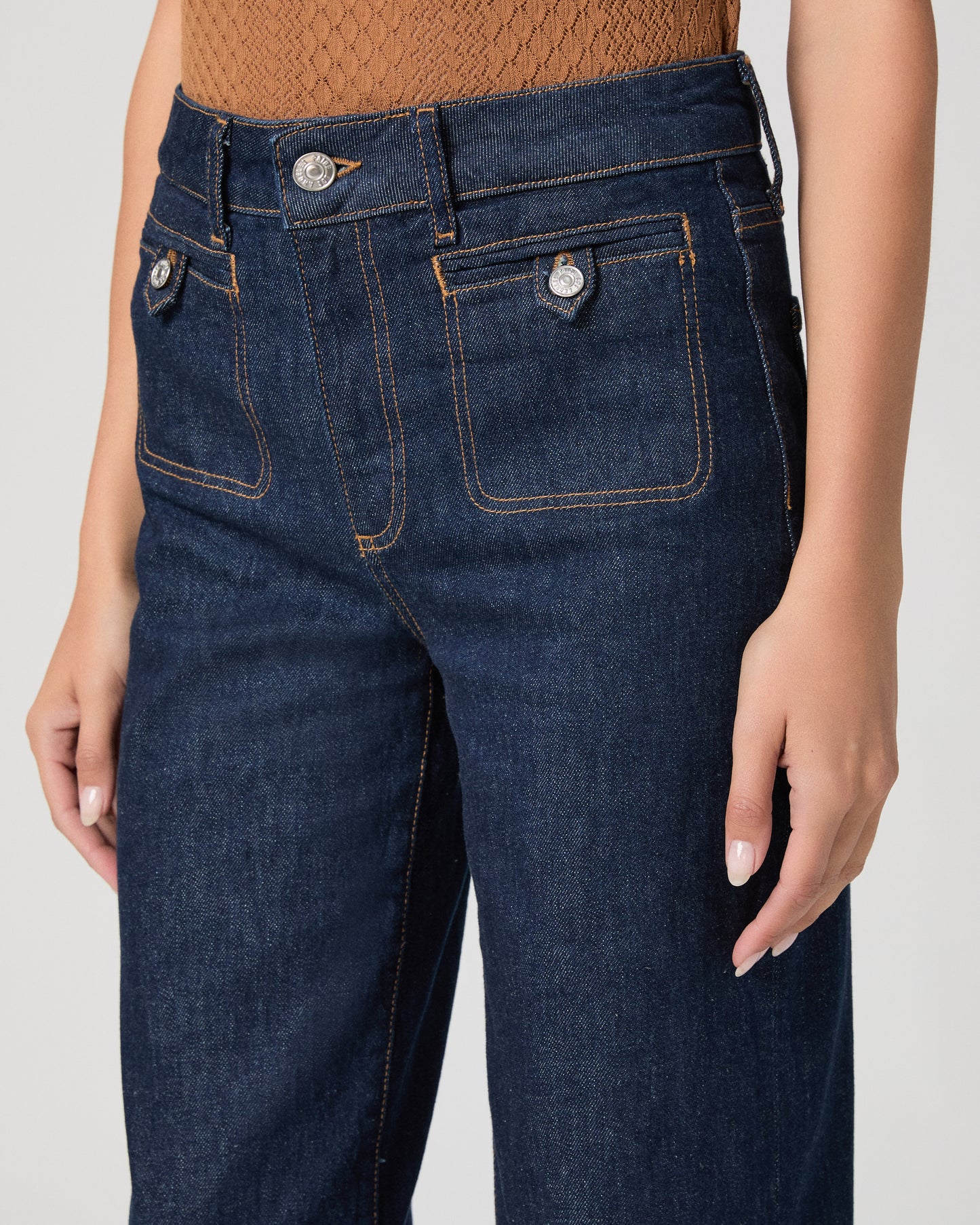Woman wearing a brown top and blue jeans on a white background