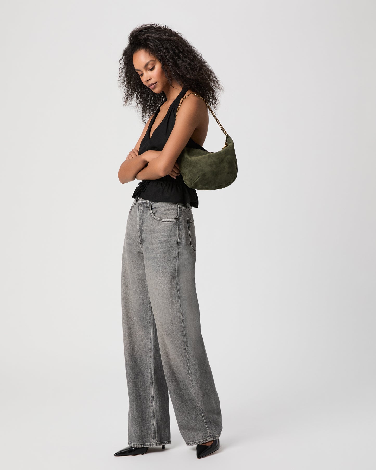 Women wearing black top paired with grey jeans holding a suede green bag against a white background
