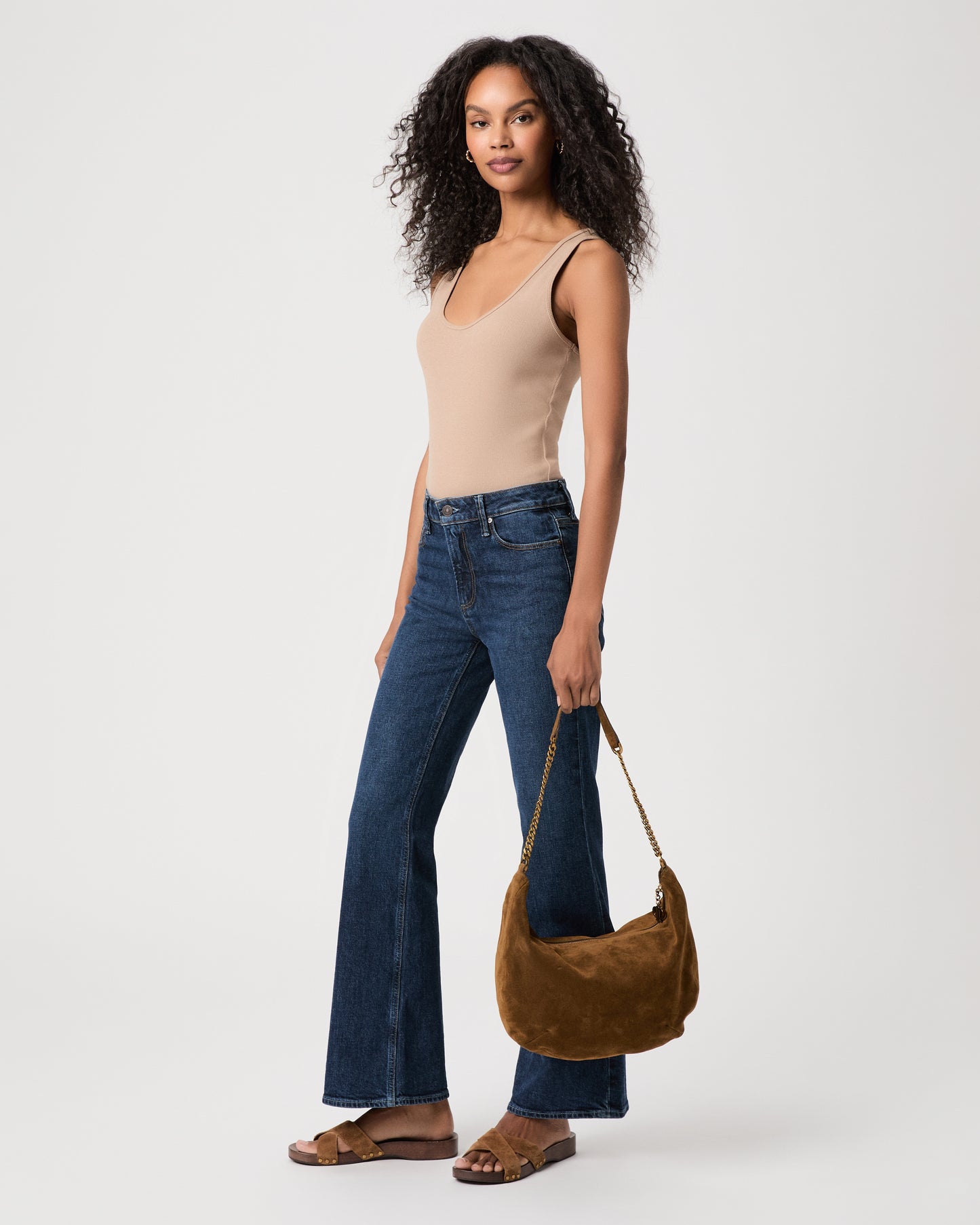 women wearing brown top Paired with blue jeans holding a brown suede bag against a white background