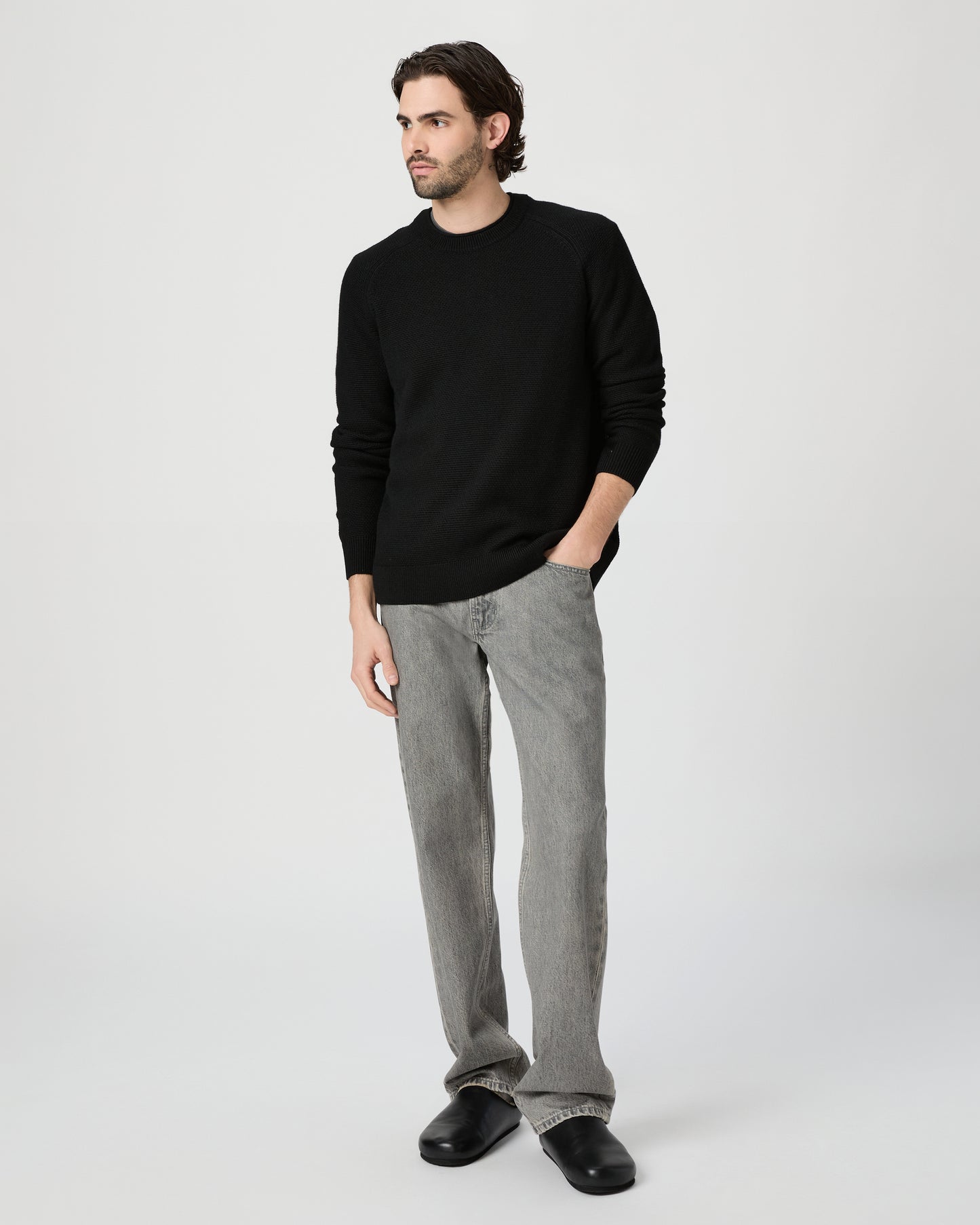 Man wearing a black sweater and gray pants on a white background