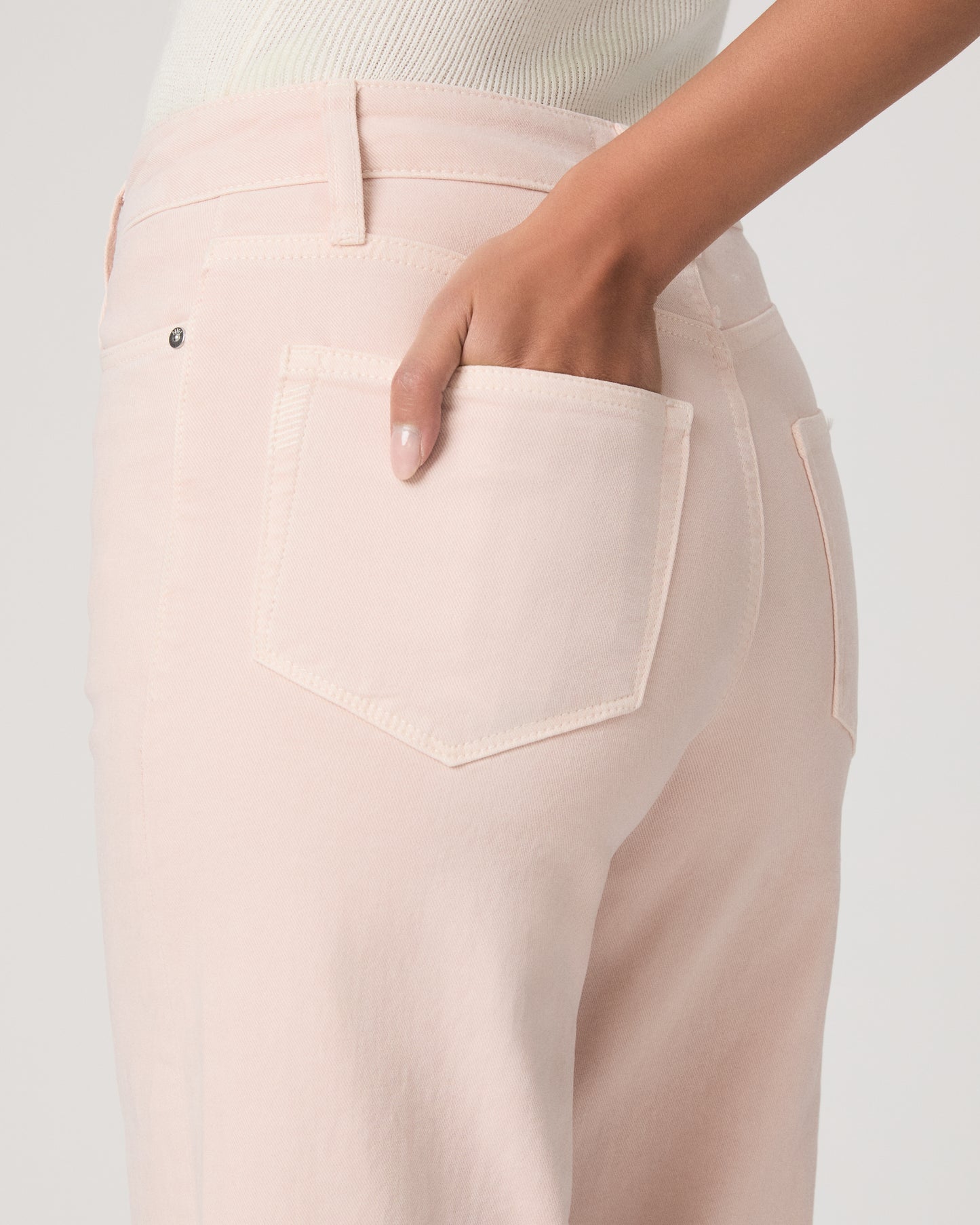 Woman wearing a white lace top, pink pants, and brown platform sandals on a light gray background