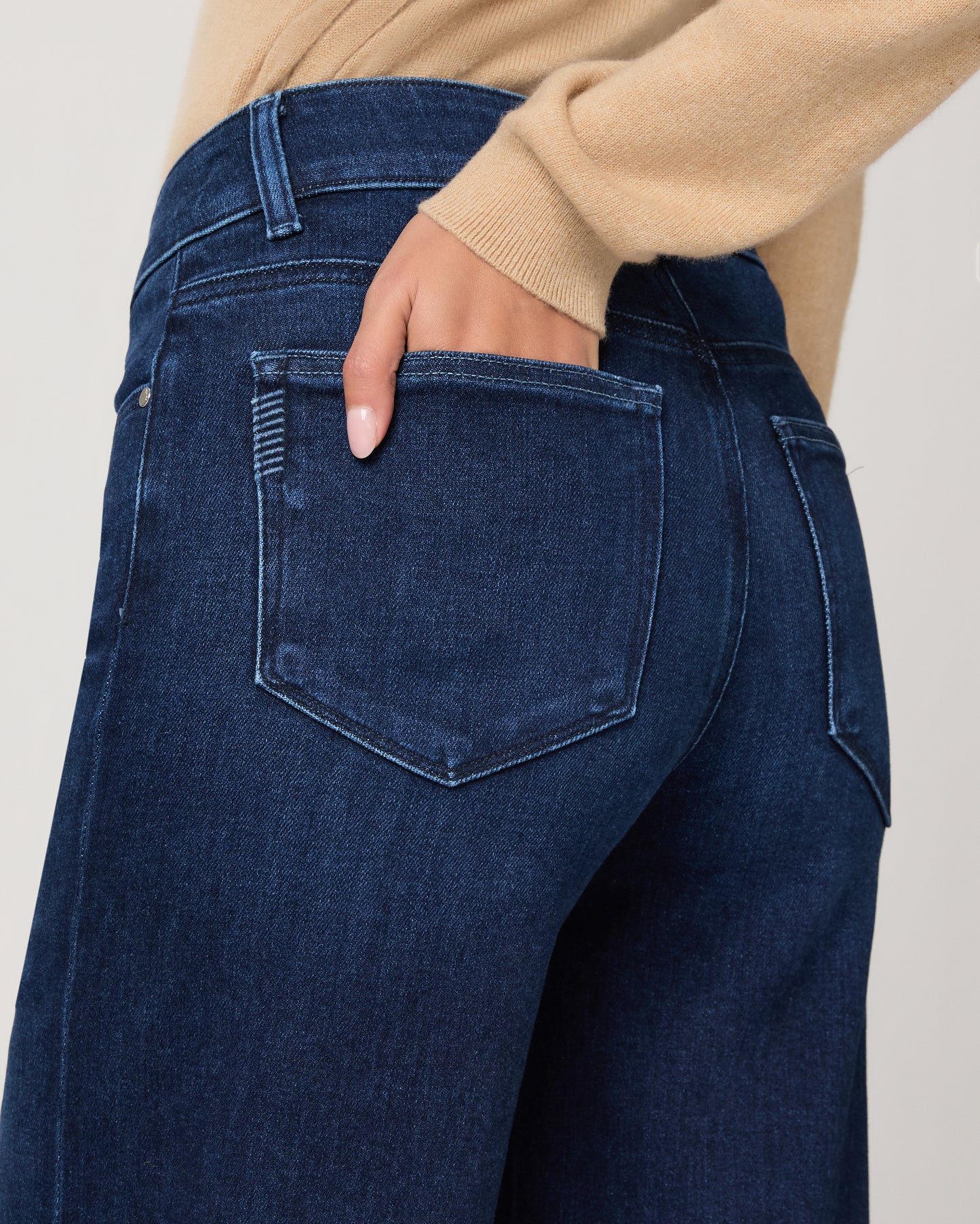 Woman wearing a beige cardigan and blue jeans on a white background