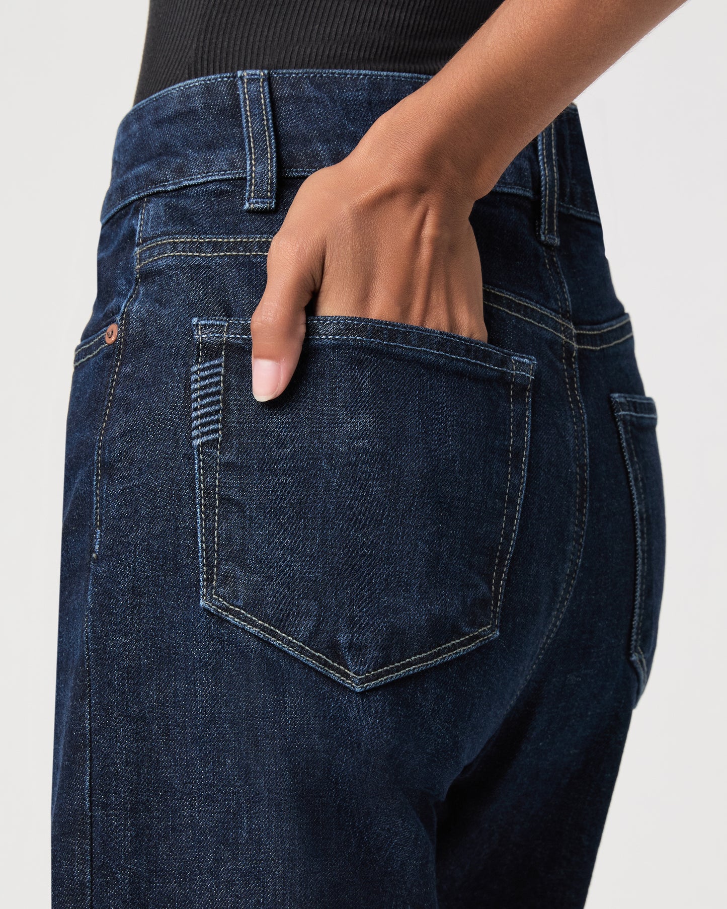 women wearing a black top paired with dark blue jeans against a white background