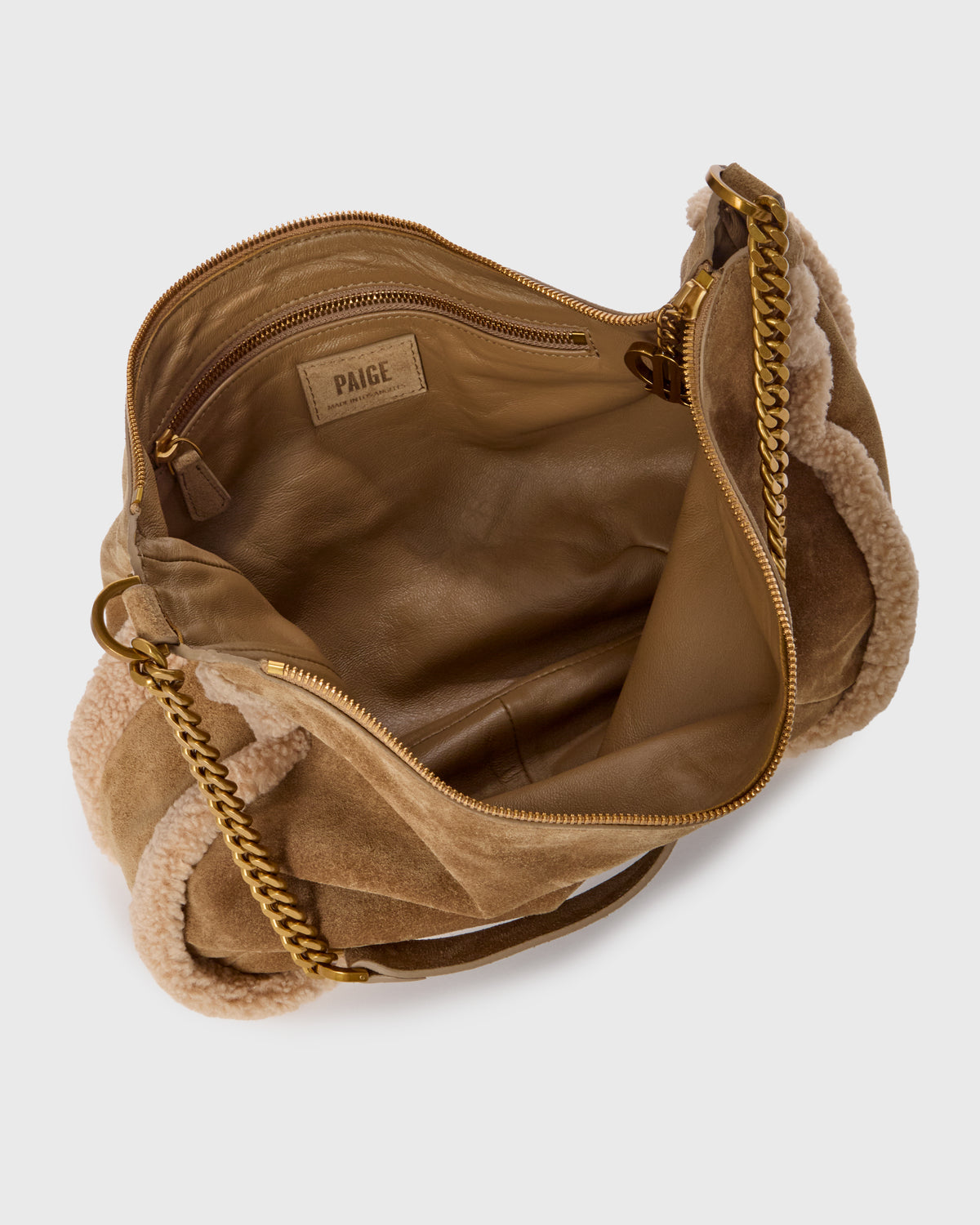 An open tan suede shoulder bag with a soft beige shearling lining, gold-tone chain strap, and a visible Paige brand label inside.