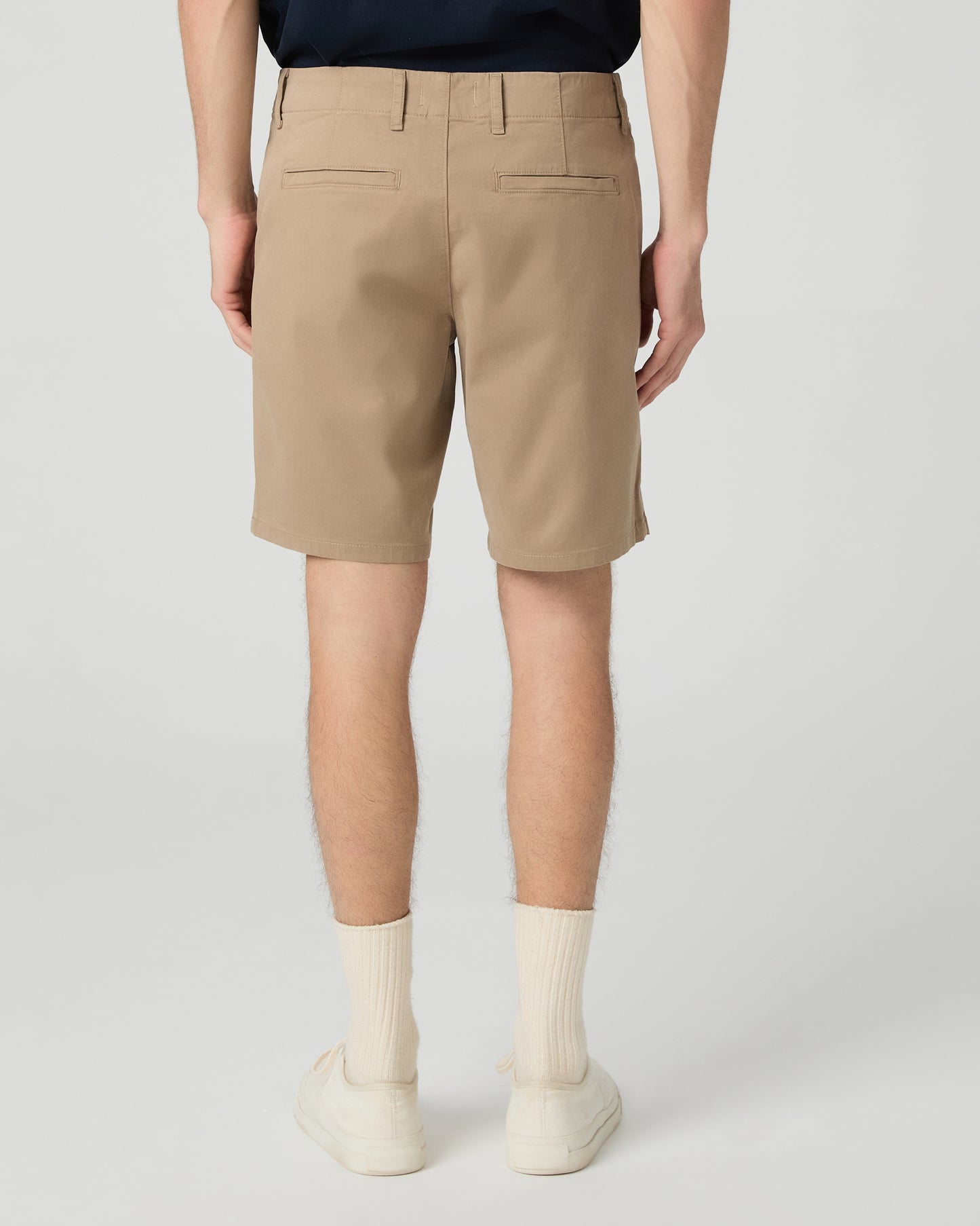 Man wearing a navy t-shirt and beige shorts on a white background