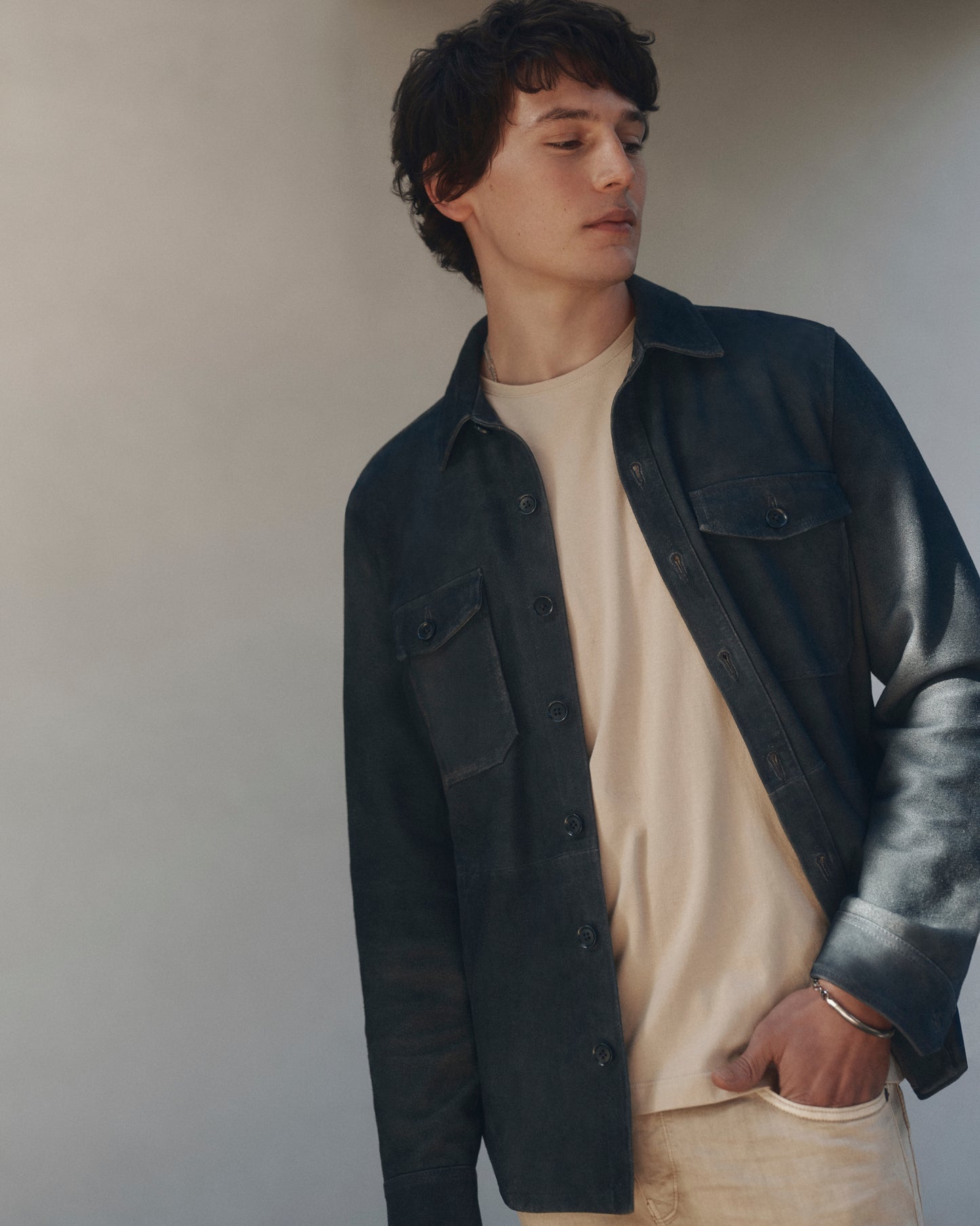 Man wearing a dark jacket over a beige shirt against a plain background