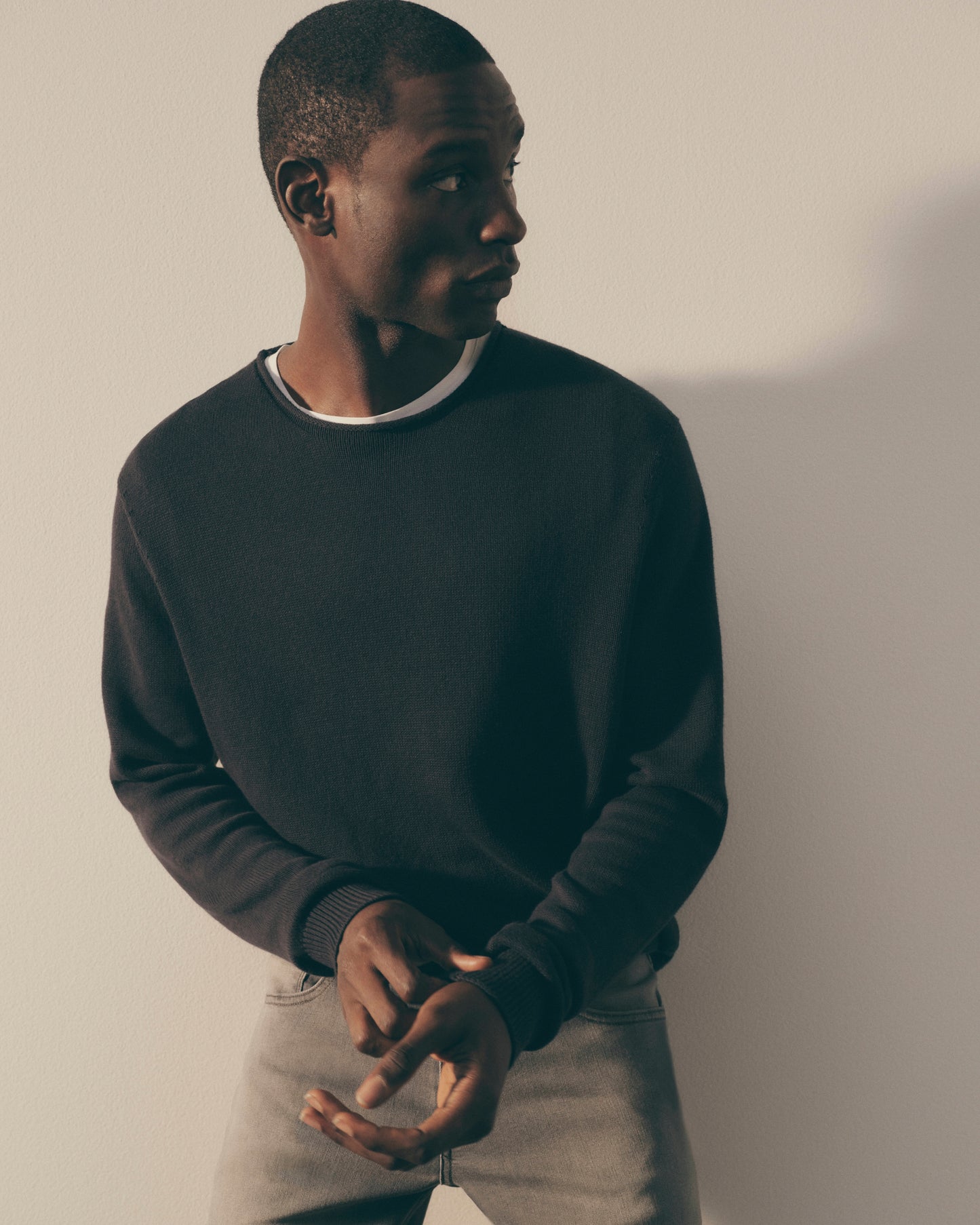Man wearing a dark sweater and light pants against a plain background