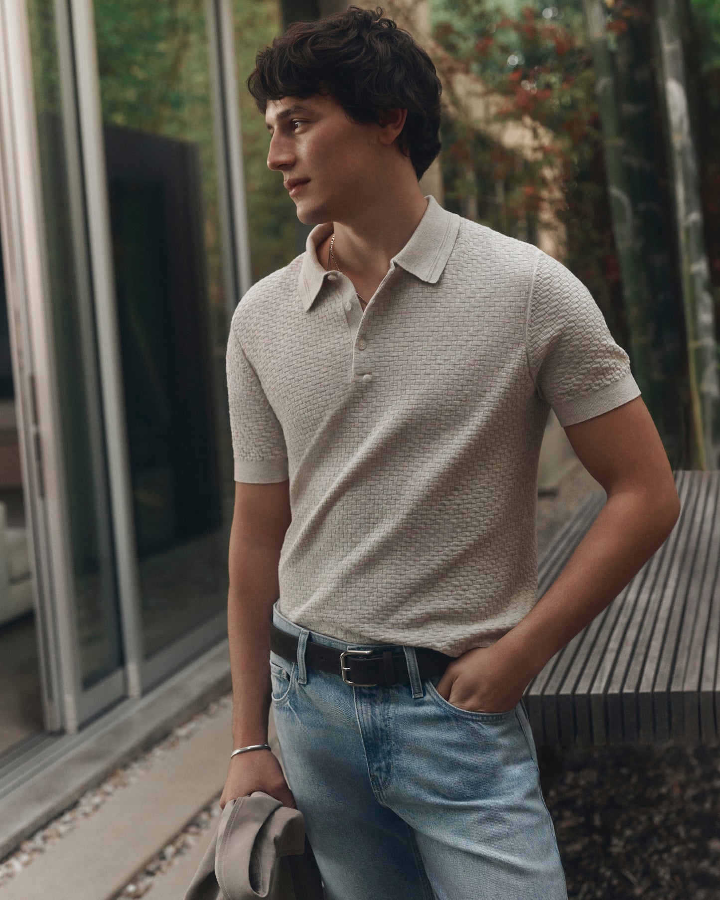 Man wearing a light gray polo shirt and blue jeans standing outdoors.
